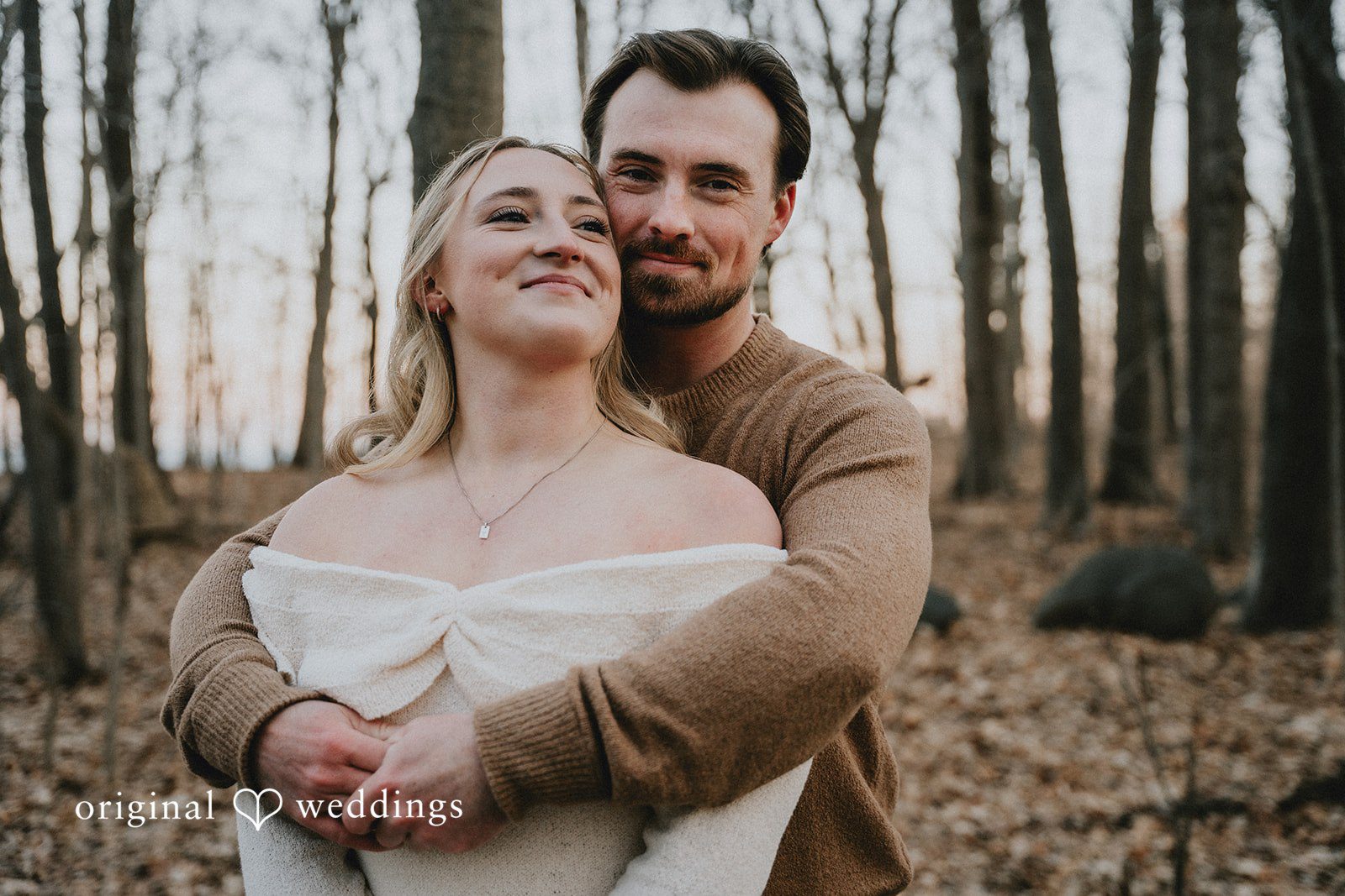 A sweet portrait of the couple leaning into each other while sitting amongst bare trees.