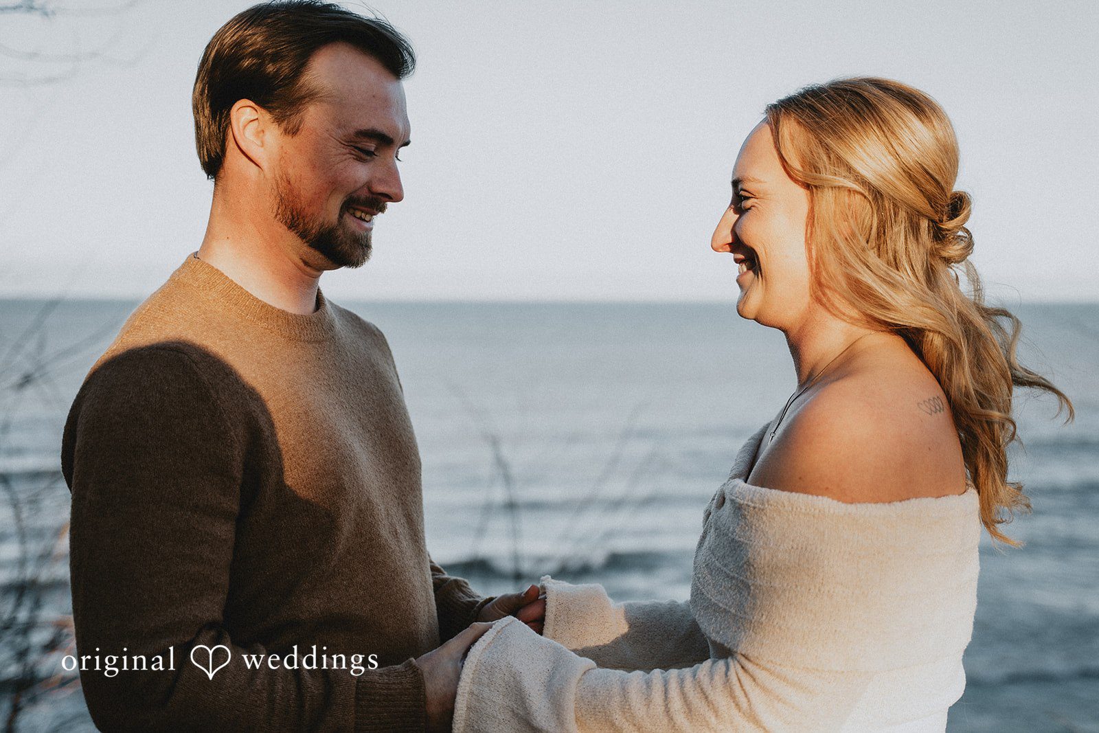 Couple facing each other and smiling while standing on a beach.