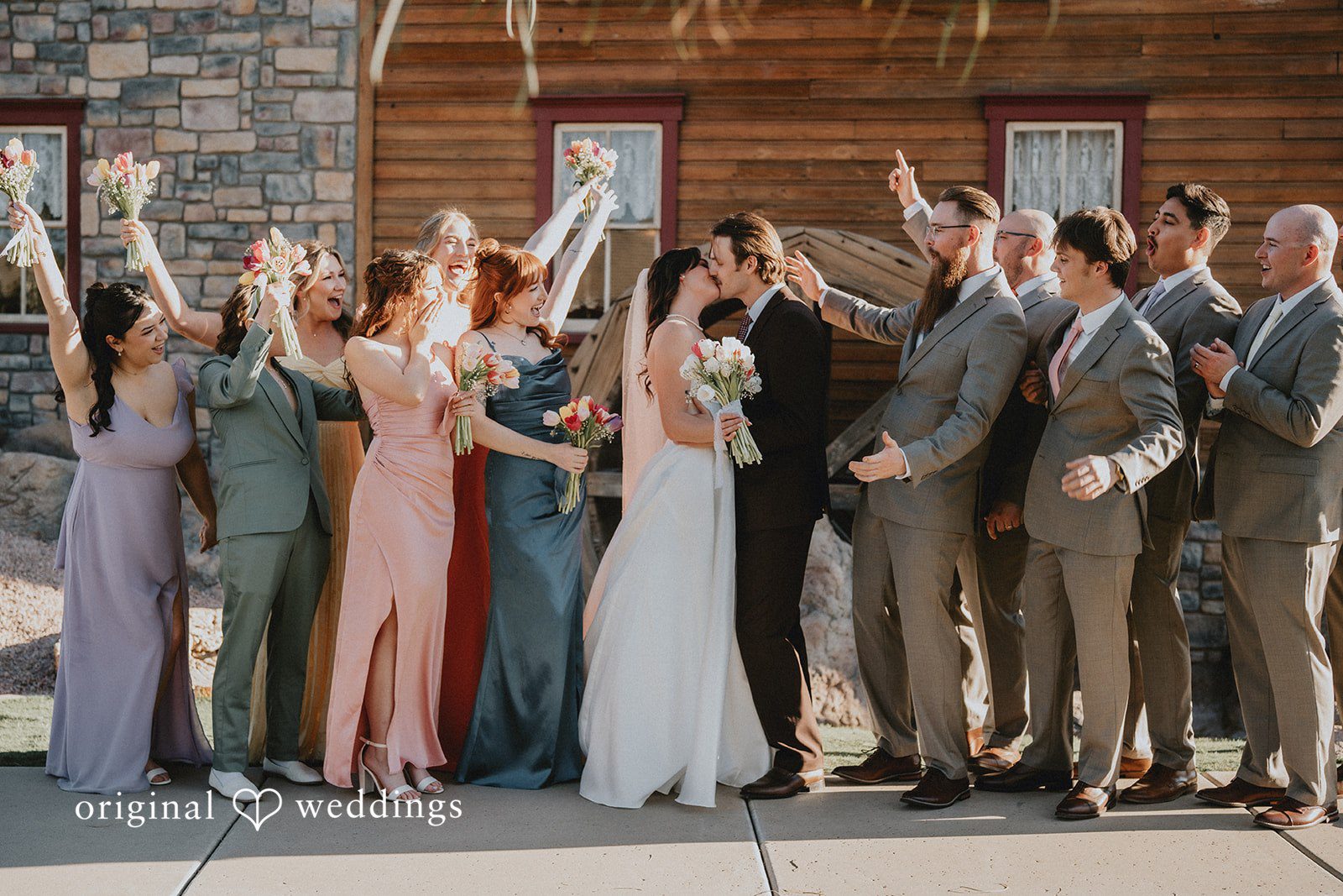 Bride and groom kissing while bridesmaids and groomsmen cheer beside them at Shenandoah Mill