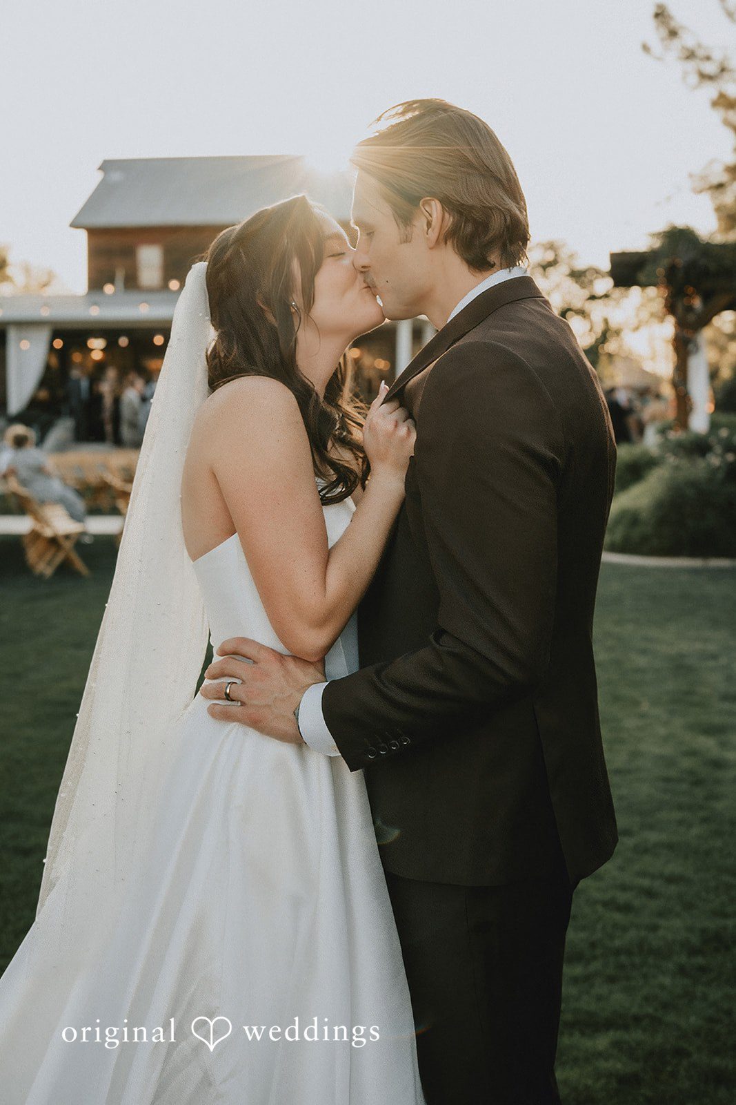 Bride and groom sharing a kiss outdoors with warm sunset light glowing behind them