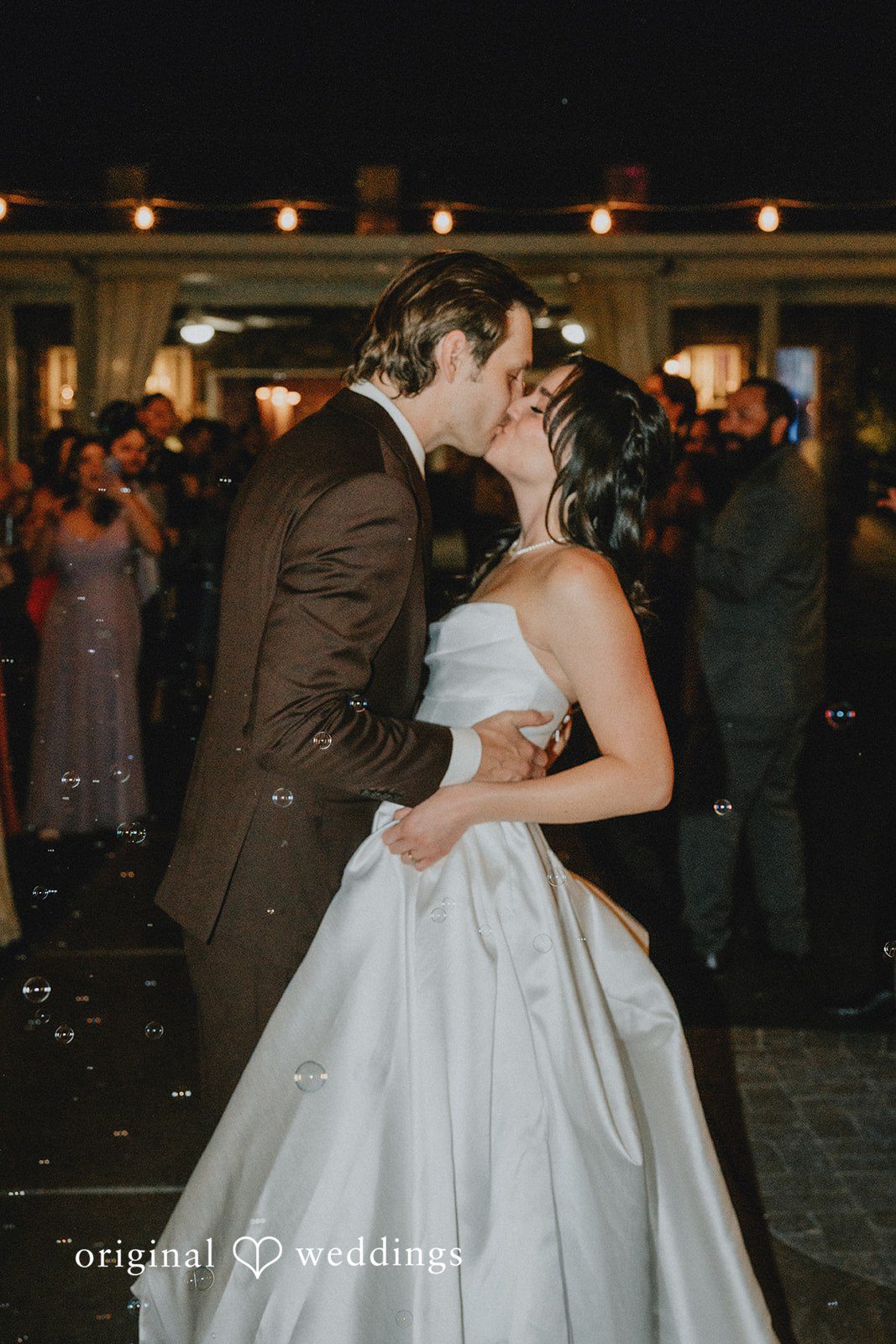 Newlywed couple kissing on the dance floor surrounded by wedding guests