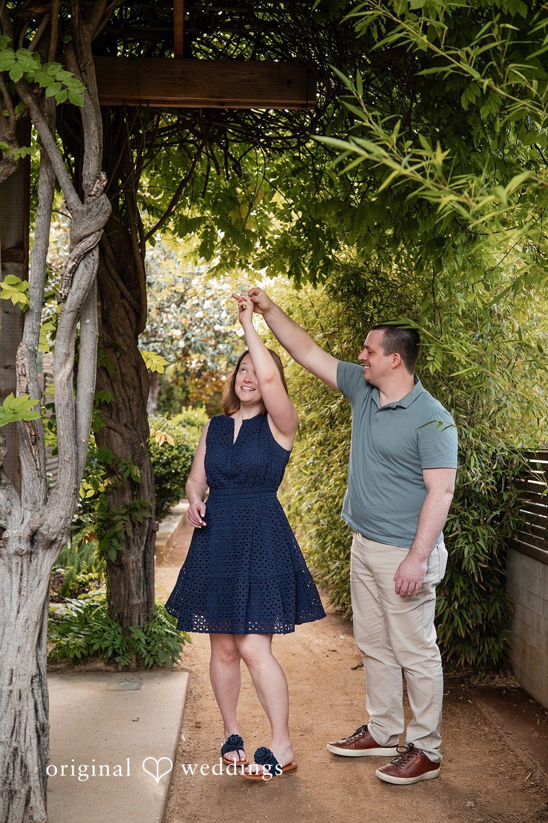 Eric + Kimberly Engaged couple twirling together beneath greenery