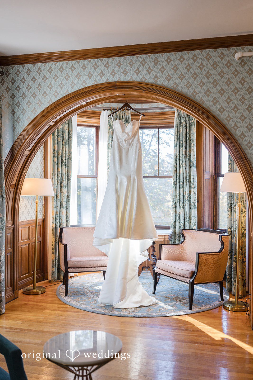 Laura + Nicholas Wedding dress hanging in an elegant historic bridal suite with arched wooden details and soft natural light at Stevens Estate at Osgood Hill
