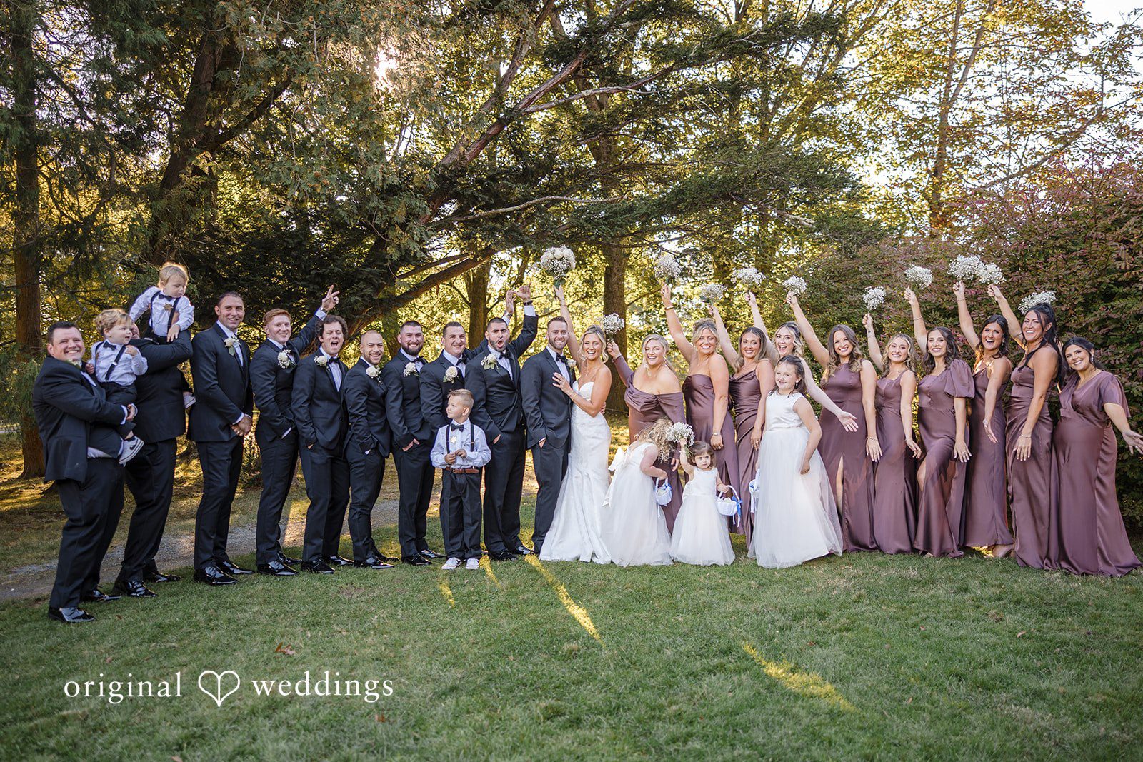 Laura + Nicholas Bride and groom posing with bridesmaids and groomsmen during joyful outdoor wedding party portrait at Stevens Estate at Osgood Hill