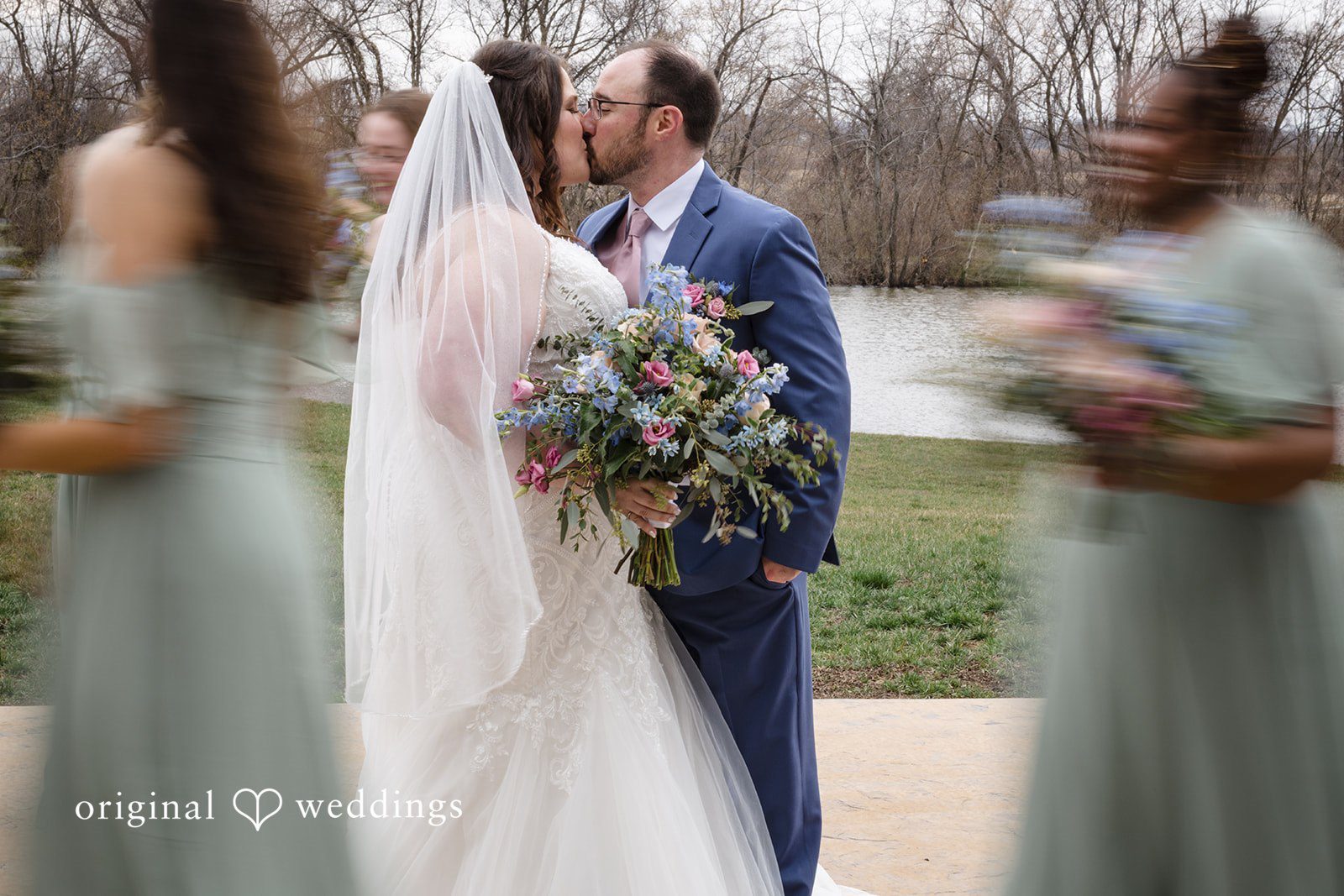 Katrena + Ryan Bride and groom sharing a kiss surrounded by the wedding party