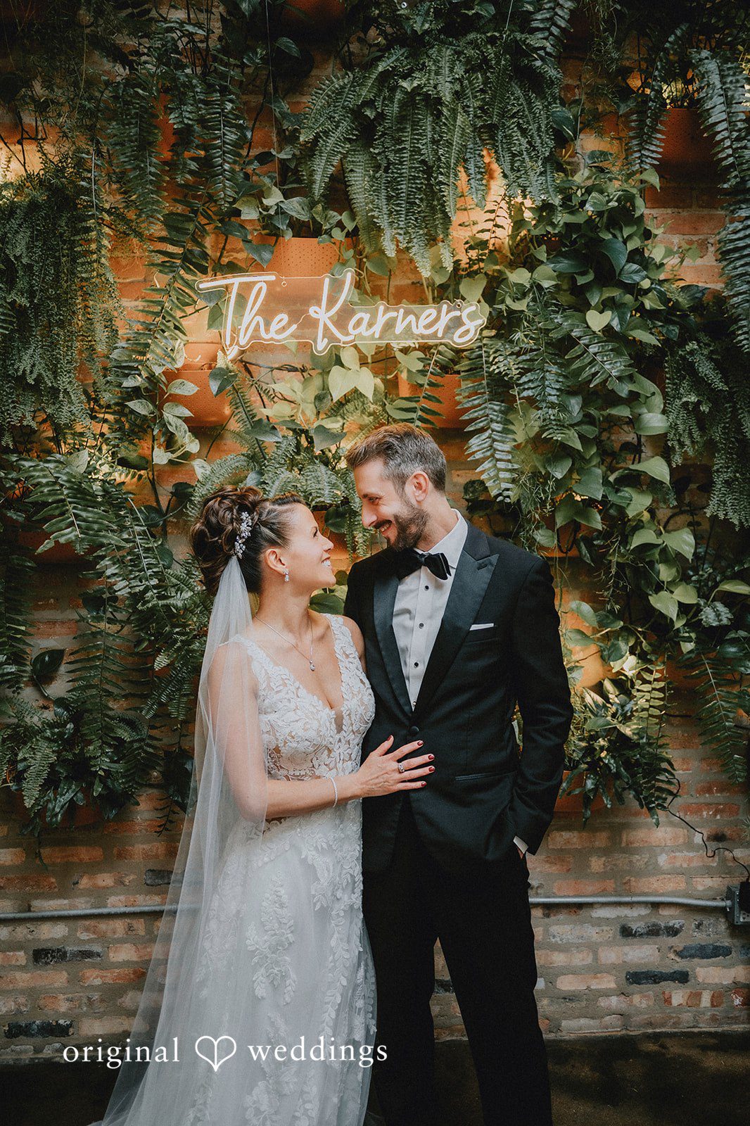 A portrait of the couple by the brick wall and greenery