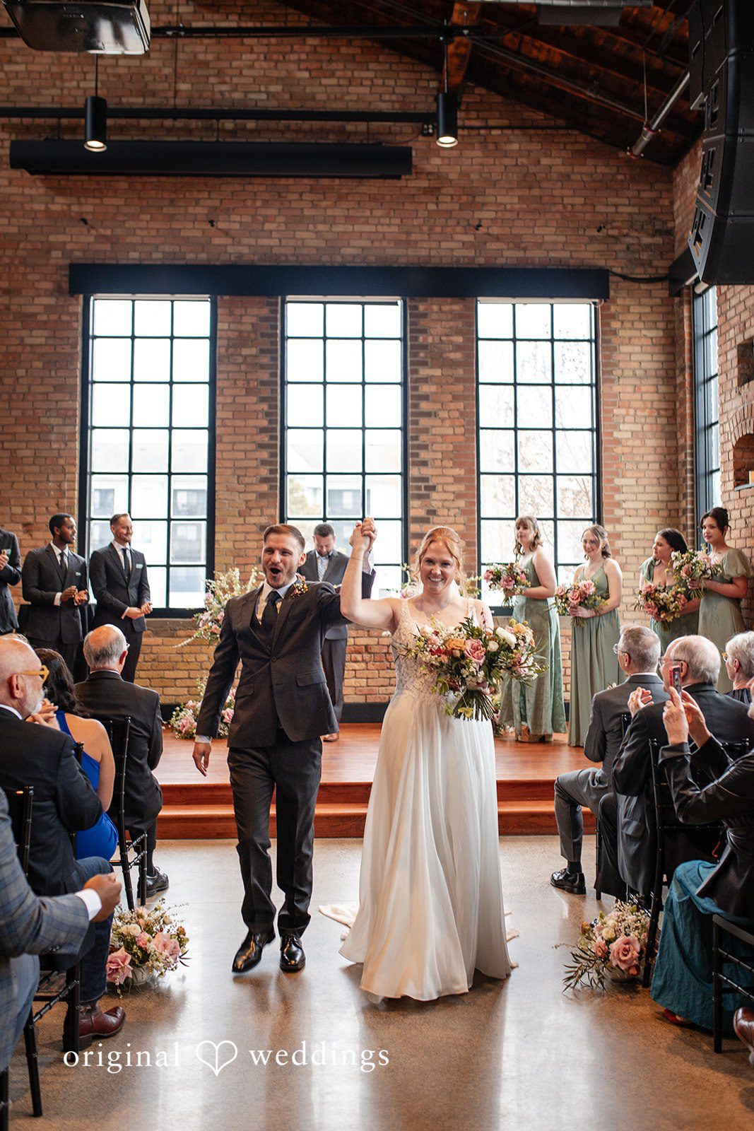 Minneapolis Wedding Photography capturing couple walking out of ceremony smiling with hands raised at The Essence Event Center by Original Weddings