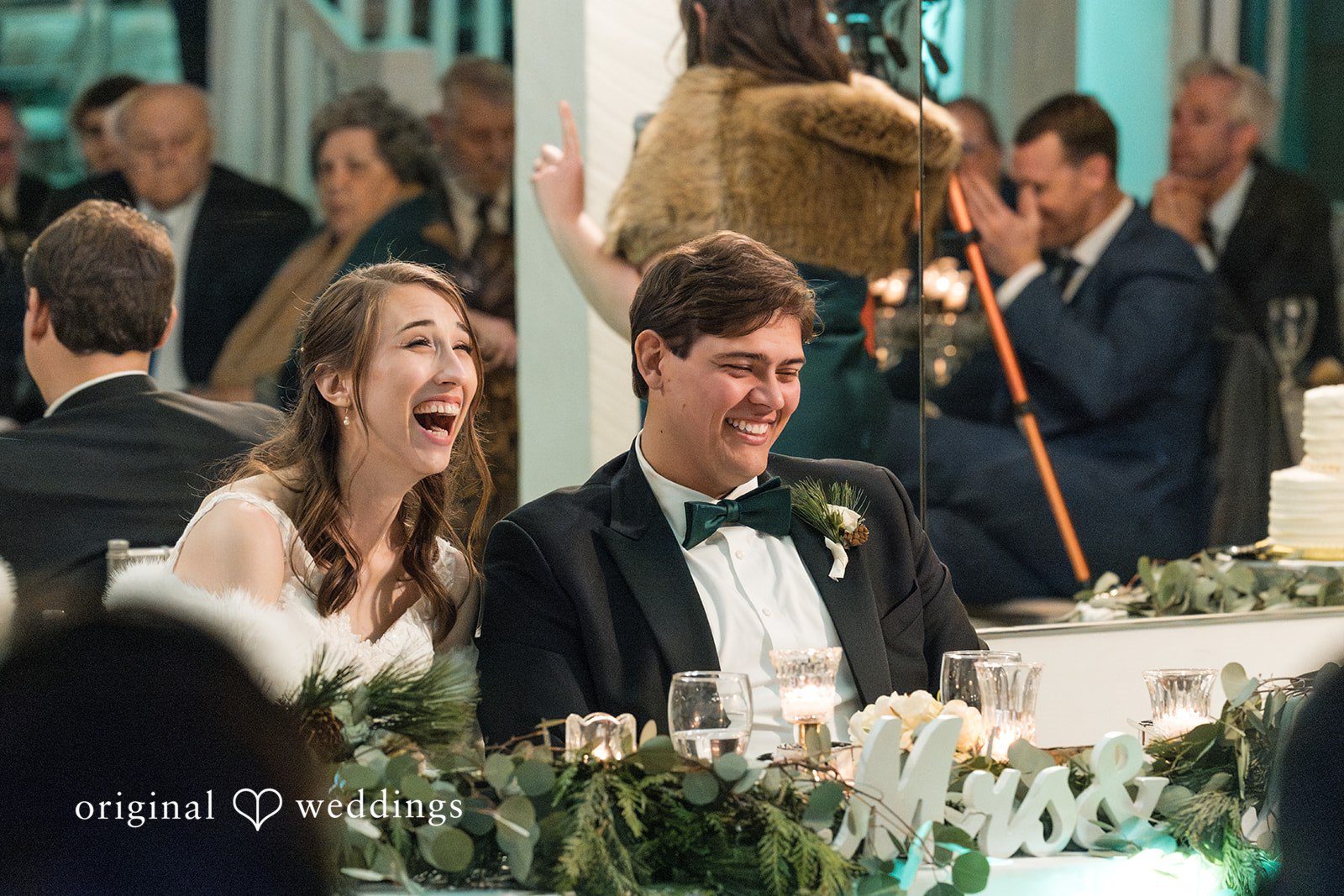 Adam + McKenzie Reception candid moment of couple seated at sweetheart table surrounded by greenery