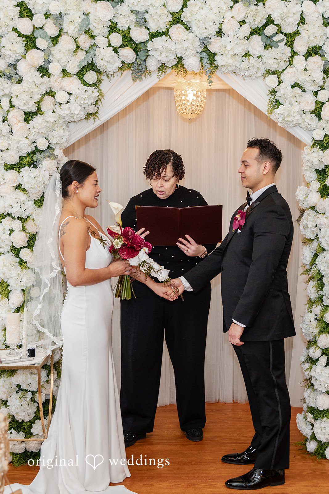 Amanda + Emmanuel Bride and groom holding hands during a ceremony in front of an officiant.