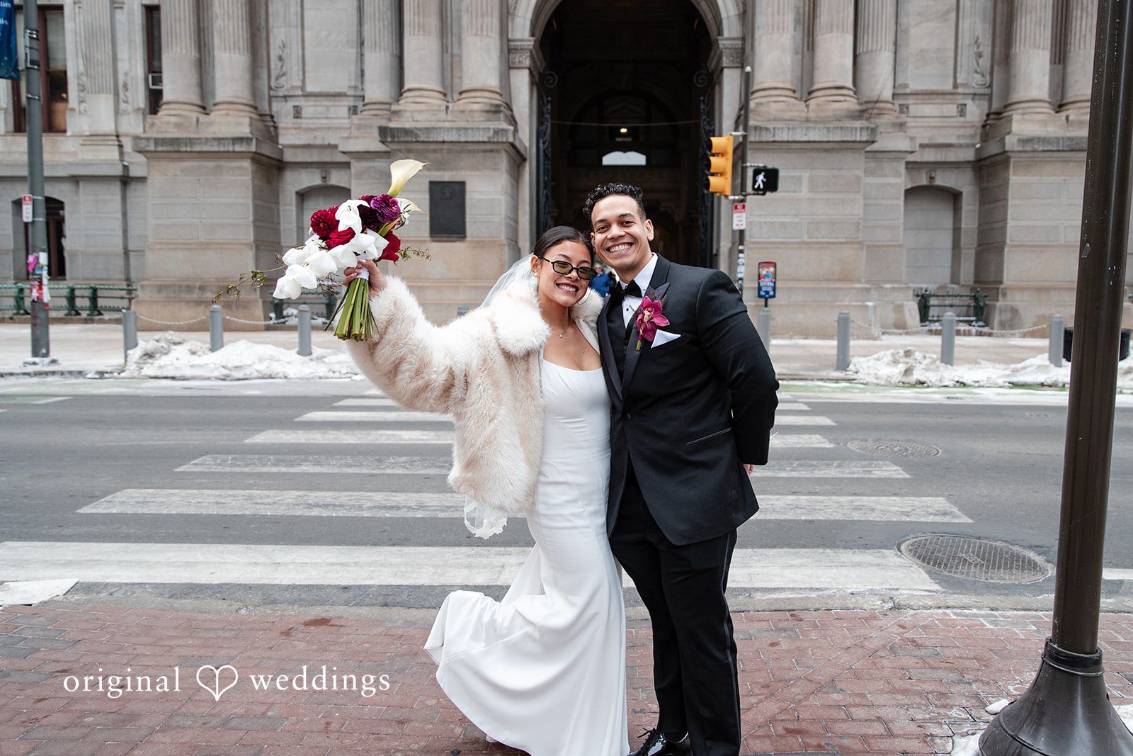 Amanda + Emmanuel Bride celebrating with raised flowers alongside the groom at a crosswalk.