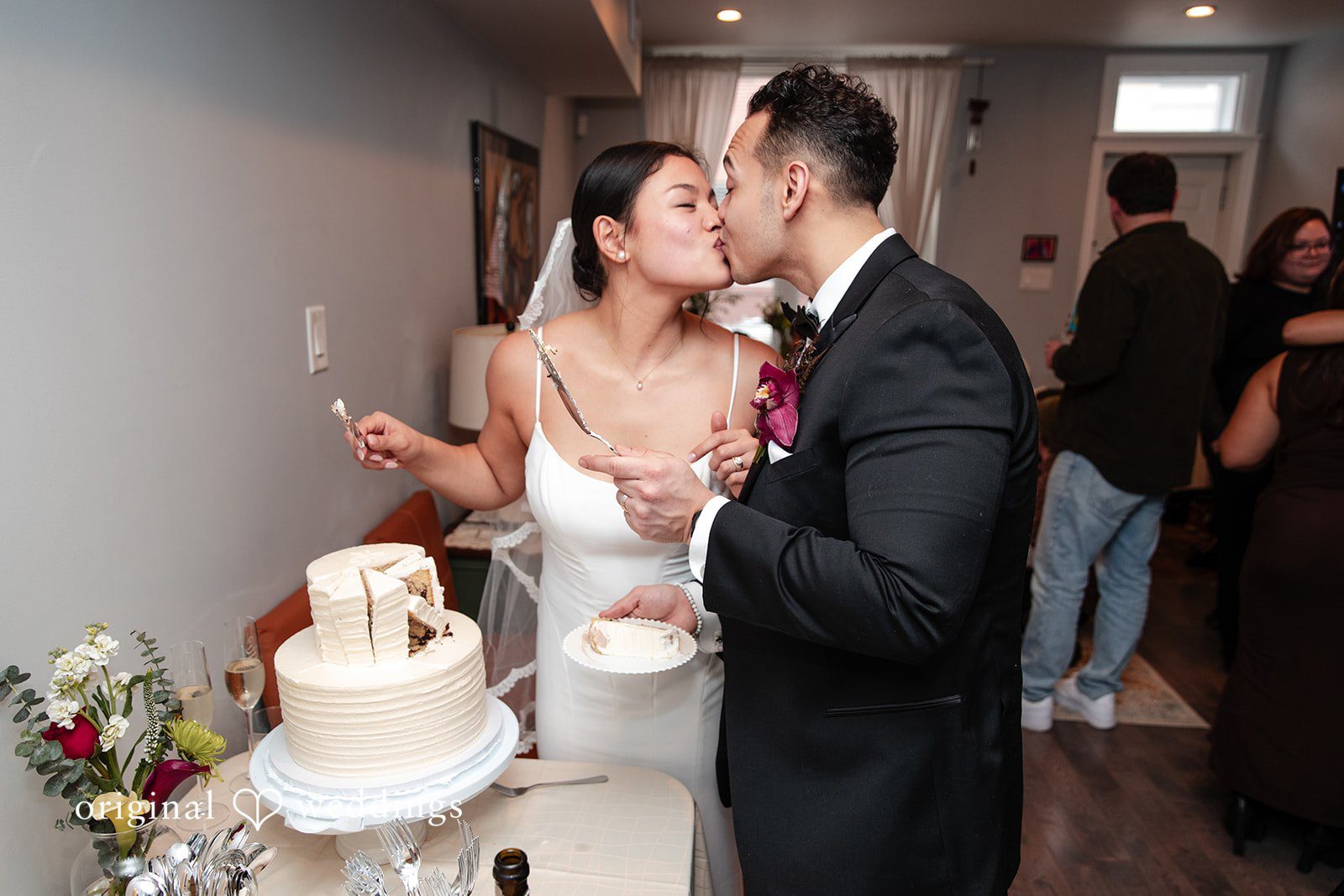 Amanda + Emmanuel Bride and groom sharing a kiss next to their wedding cake.