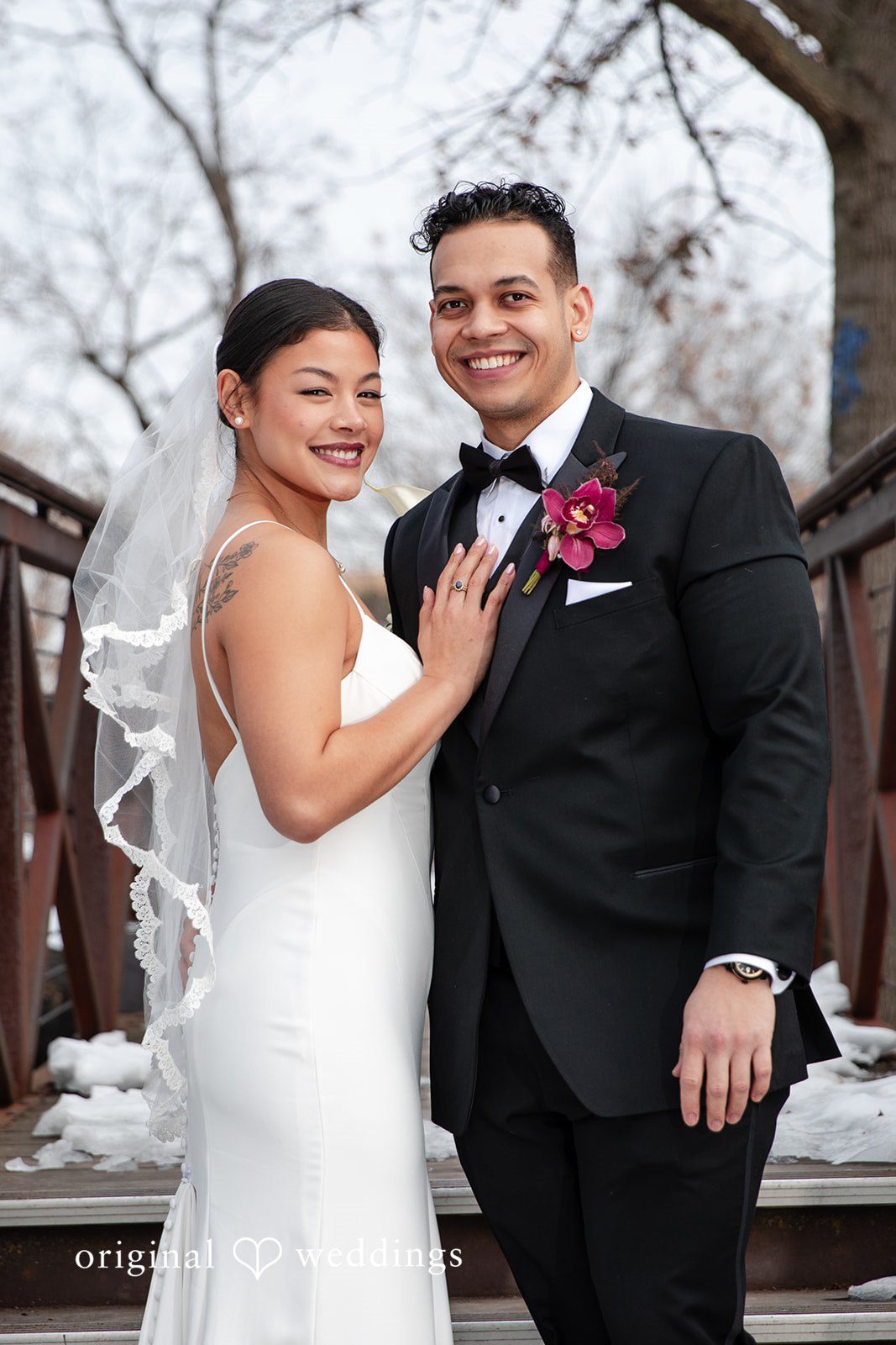 Amanda + Emmanuel Bride and groom posing closely together with a bridge structure behind them.