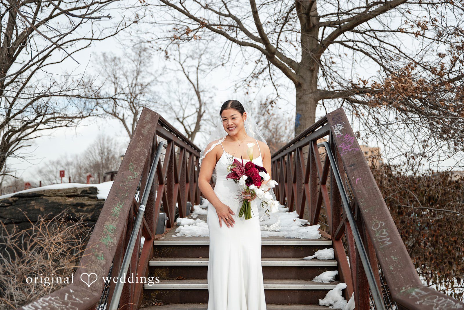 Amanda + Emmanuel Bride holding a bouquet and posing on a wooden bridge structure.