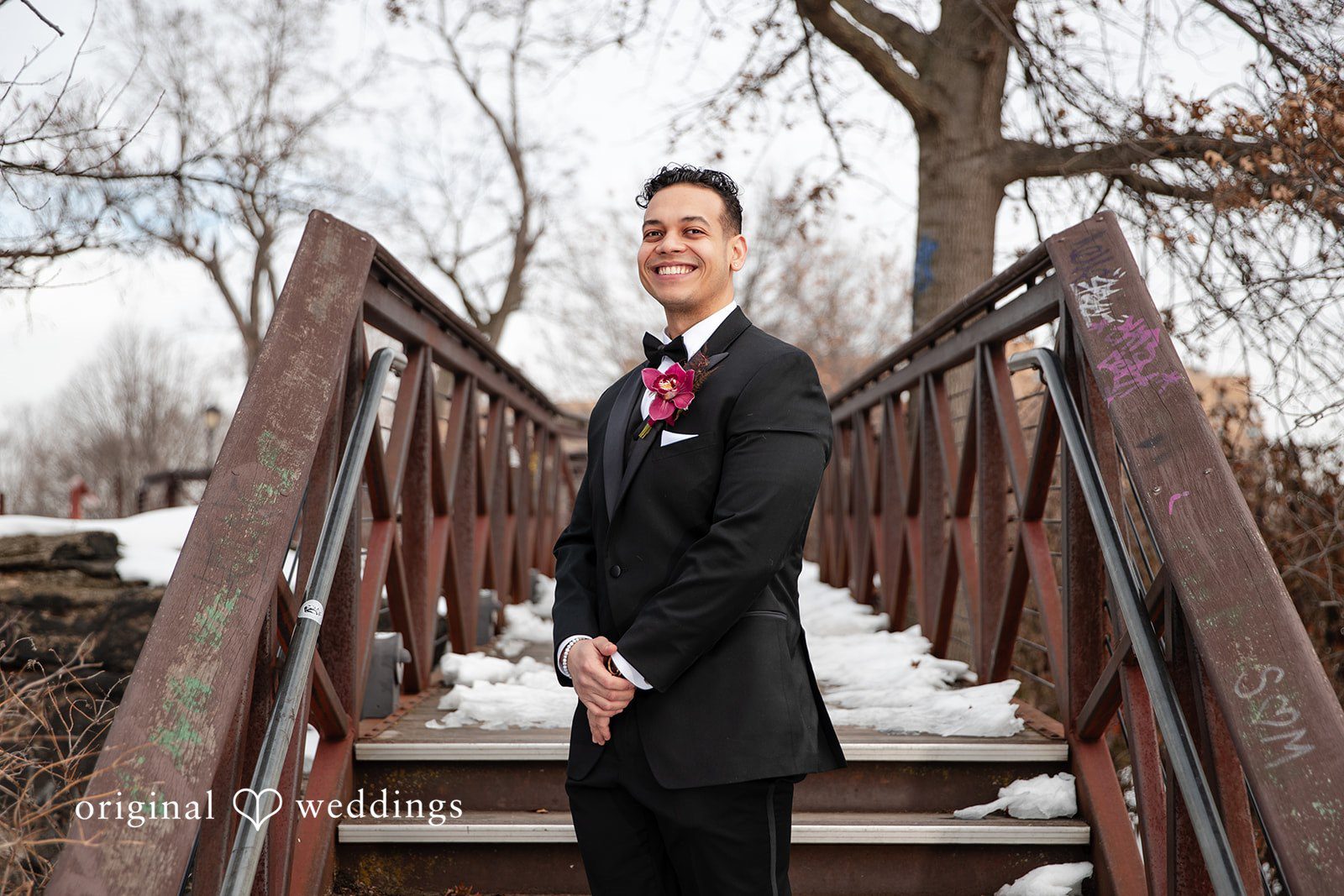 Amanda + Emmanuel Groom wearing a dark suit posing on a wooden bridge structure.
