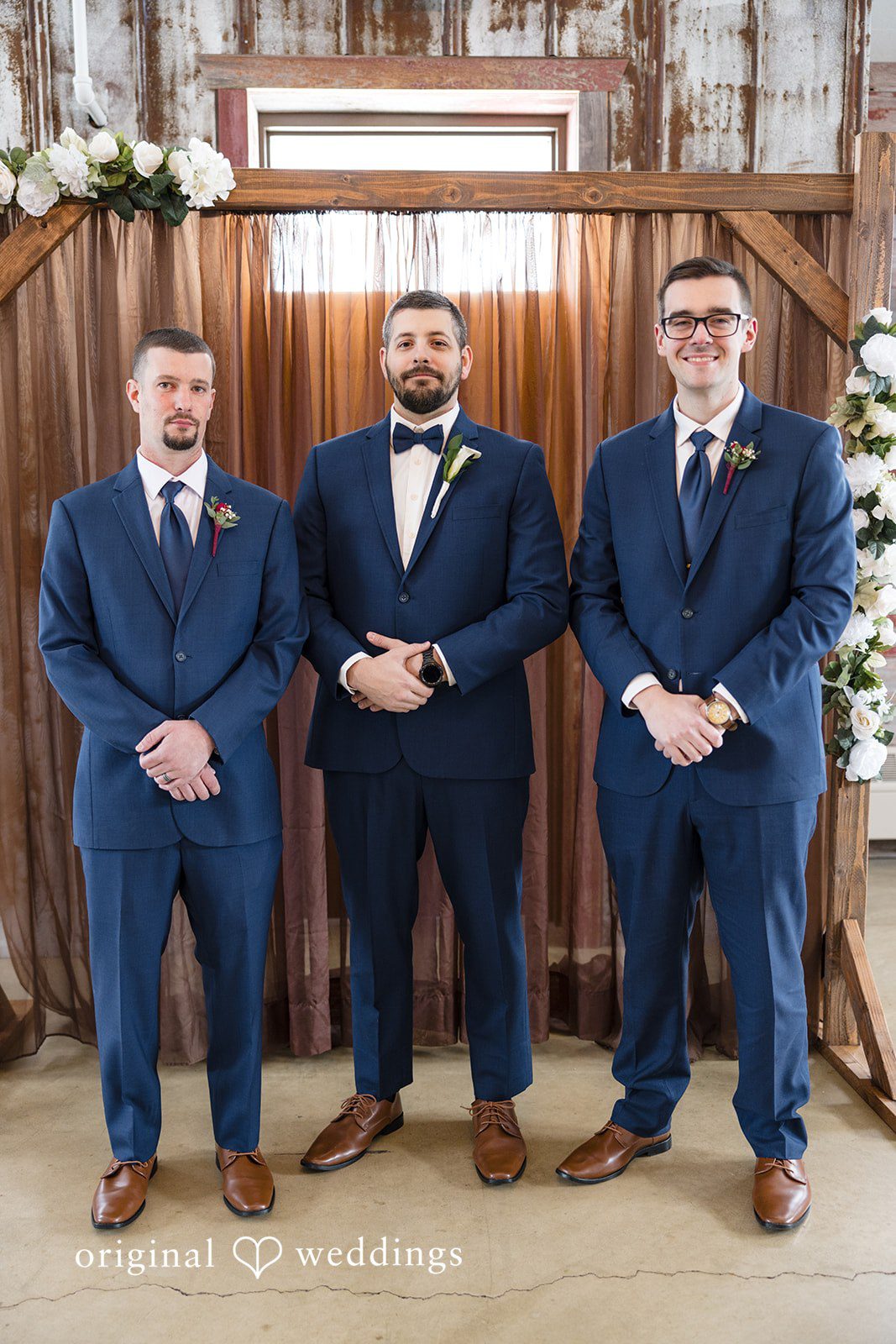 Alia + Lance Groom standing with two groomsmen in matching navy blue suits at the village barn.
