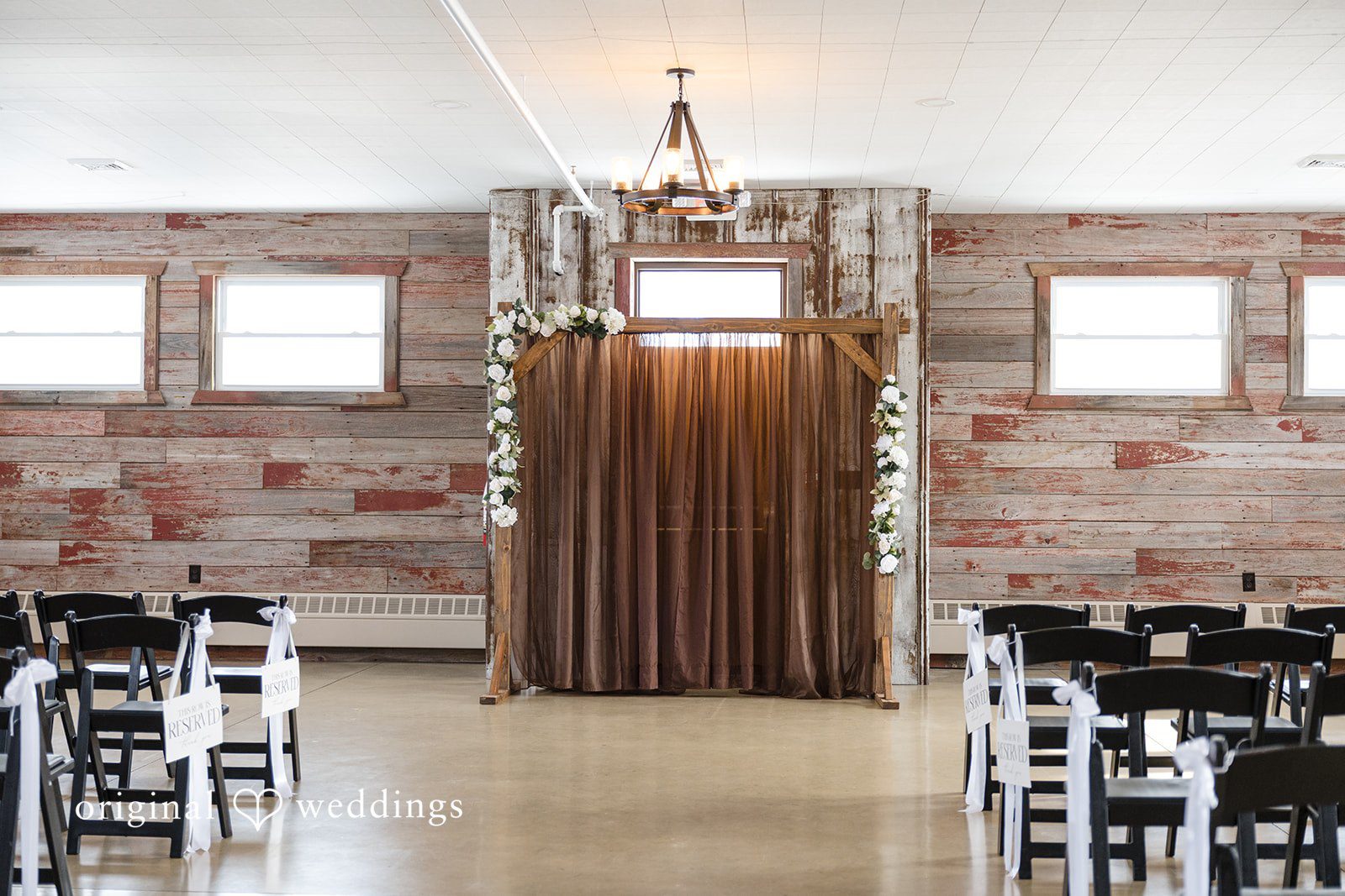 Alia + Lance Empty wedding ceremony aisle with a brown fabric backdrop and rows of black chairs.