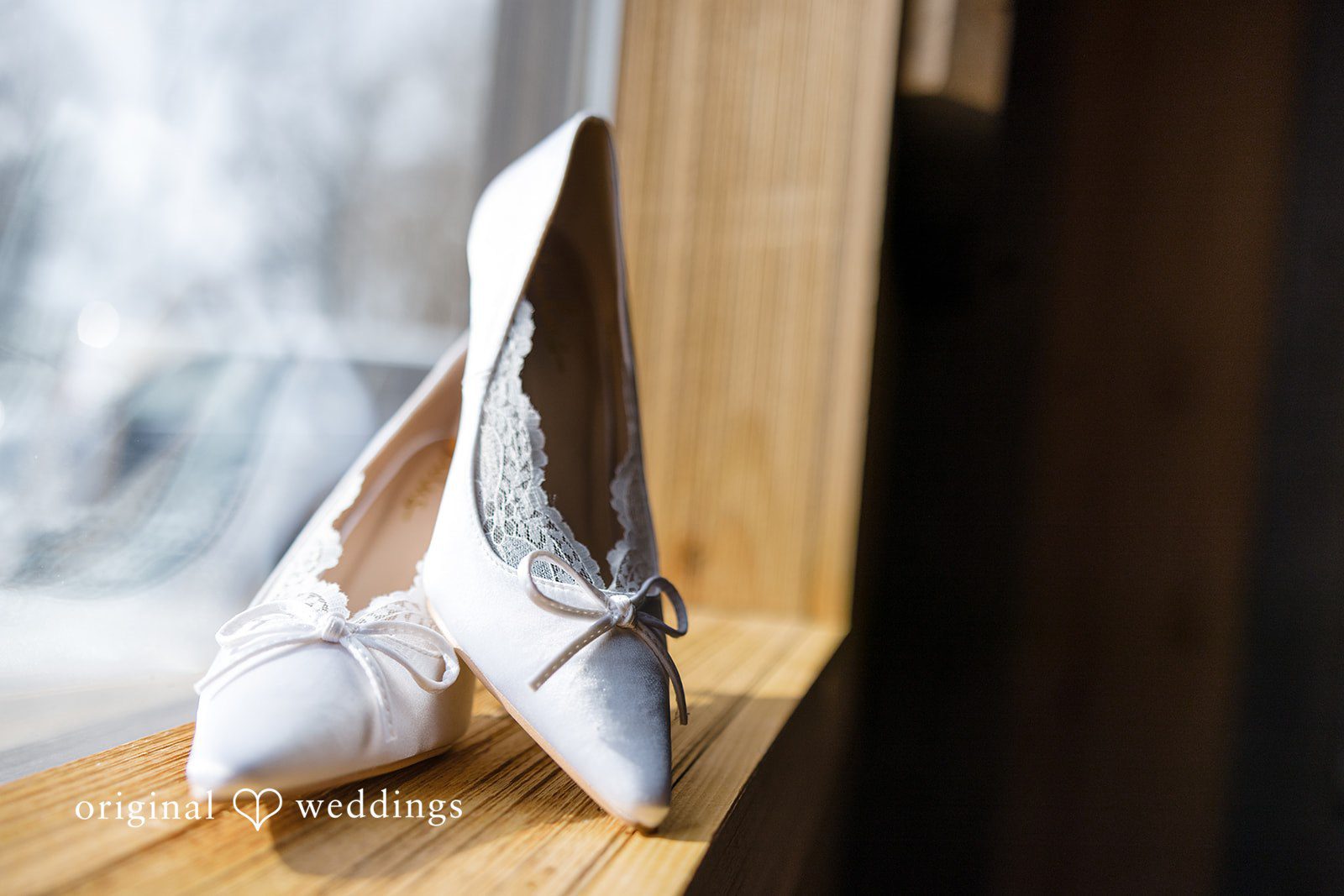 Alia + Lance Pair of white bridal high heel shoes hanging from a wooden beam.