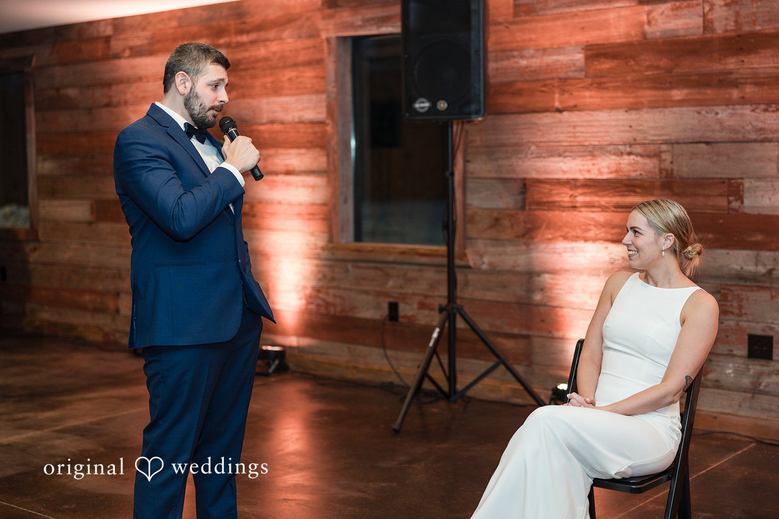 Alia + Lance Groom giving a speech into a microphone while the bride listens.