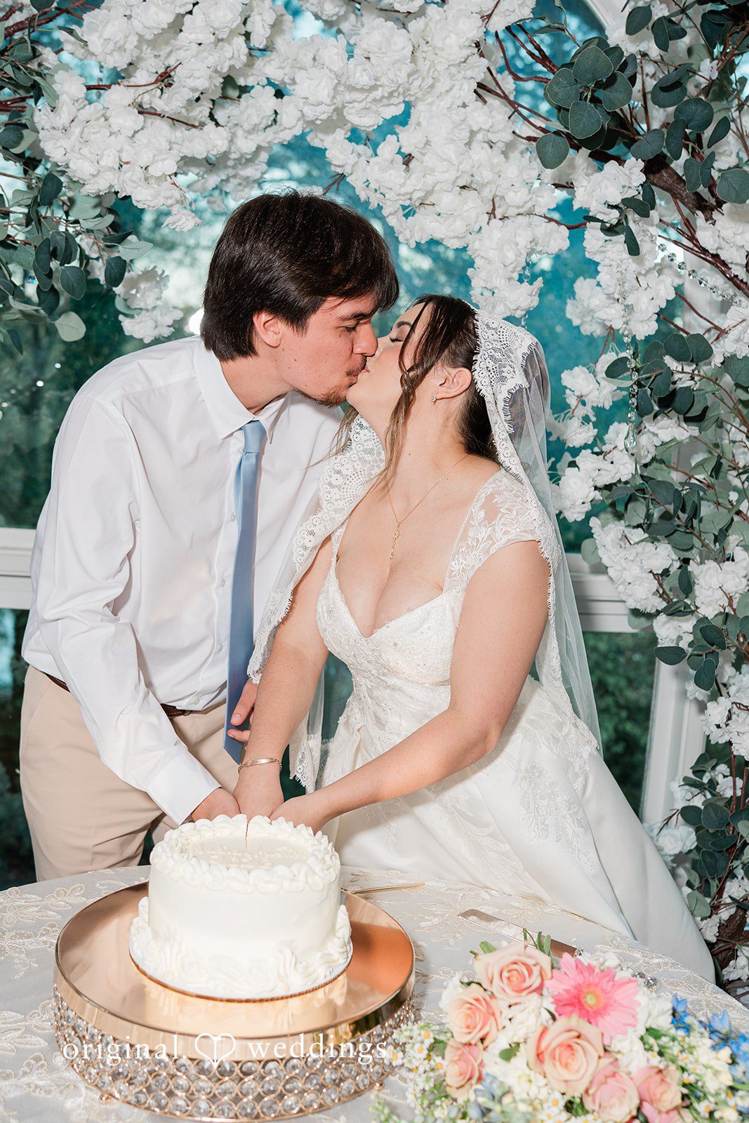 Elegant couple sharing kiss while cutting wedding cake