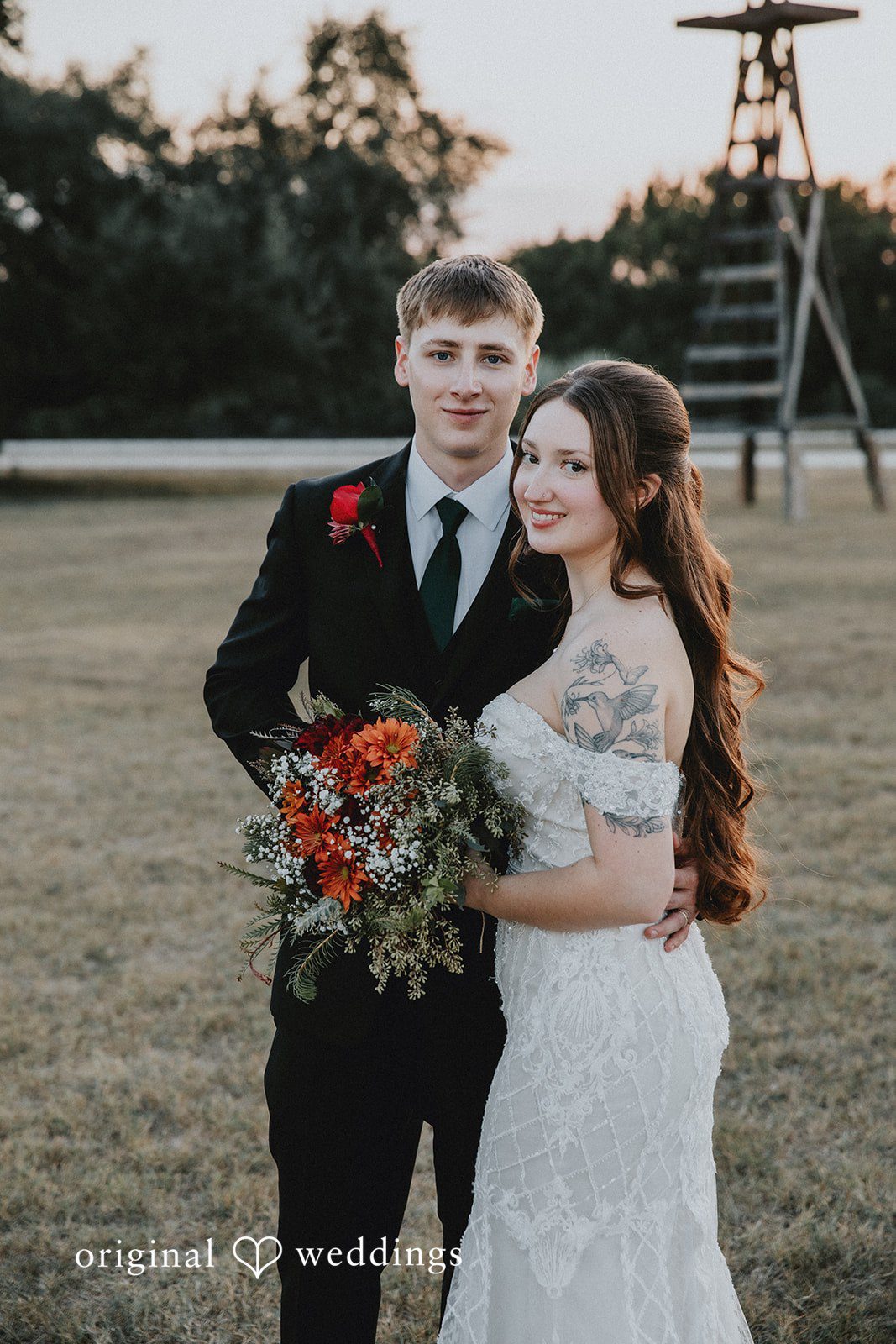 Newlywed couple posing together in a grassy field holding a bouquet during golden hour wedding portraits