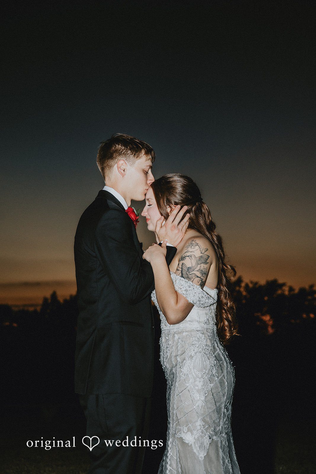 Groom kissing bride on the forehead during romantic sunset wedding portrait outdoors