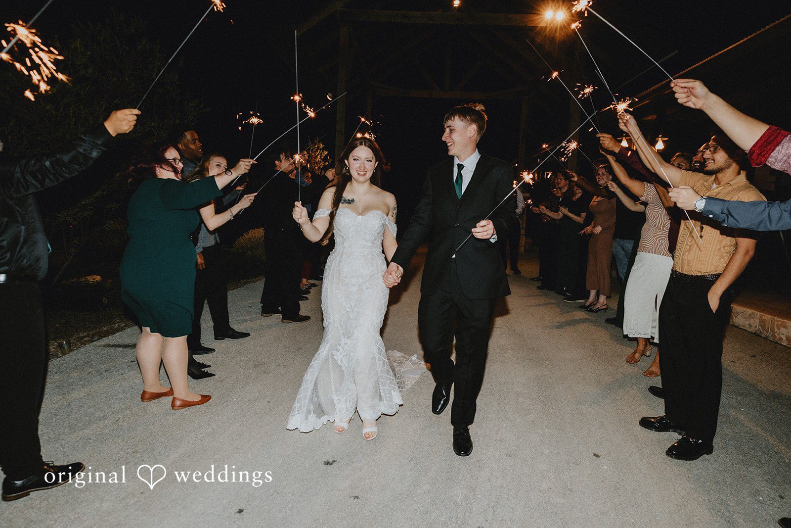Newlywed couple celebrating wedding send off with guests holding sparklers outdoors