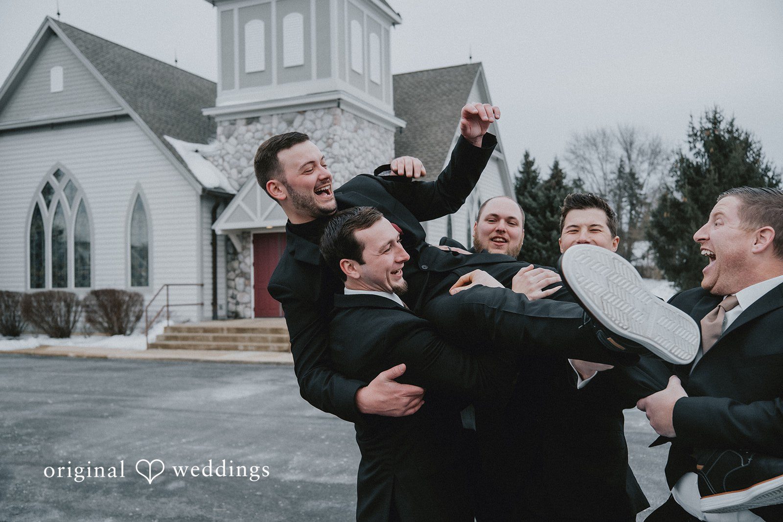Sarah + Justin Groom being lifted in celebration by groomsmen with joyful energy.