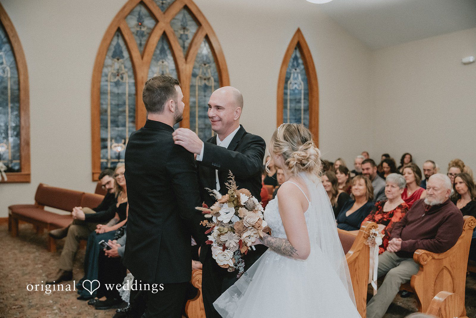 Sarah + Justin A man pats the groom's shoulder while handing off the bride at the altar during a church wedding.