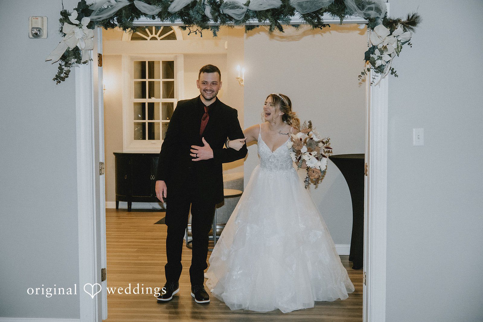 Sarah + Justin A laughing bride and smiling groom make their entrance under a green garland archway.