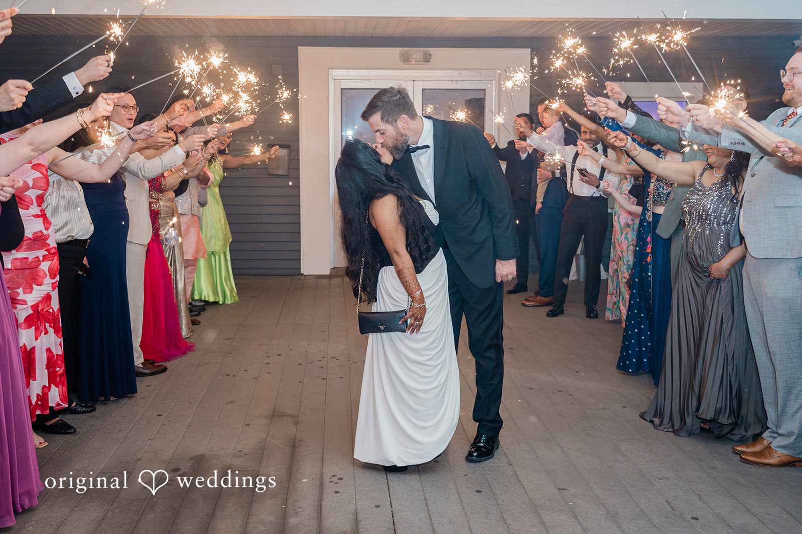 Bride and groom sharing a romantic kiss while guests cheering around