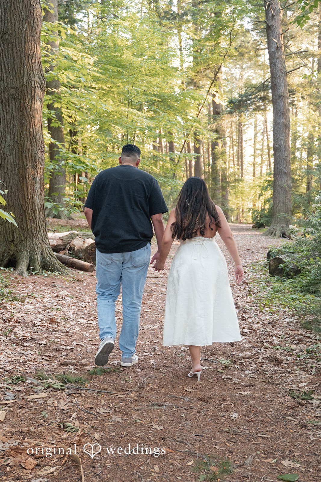 Anya + Max Couple walks hand in hand along a peaceful wooded path during their engagement session