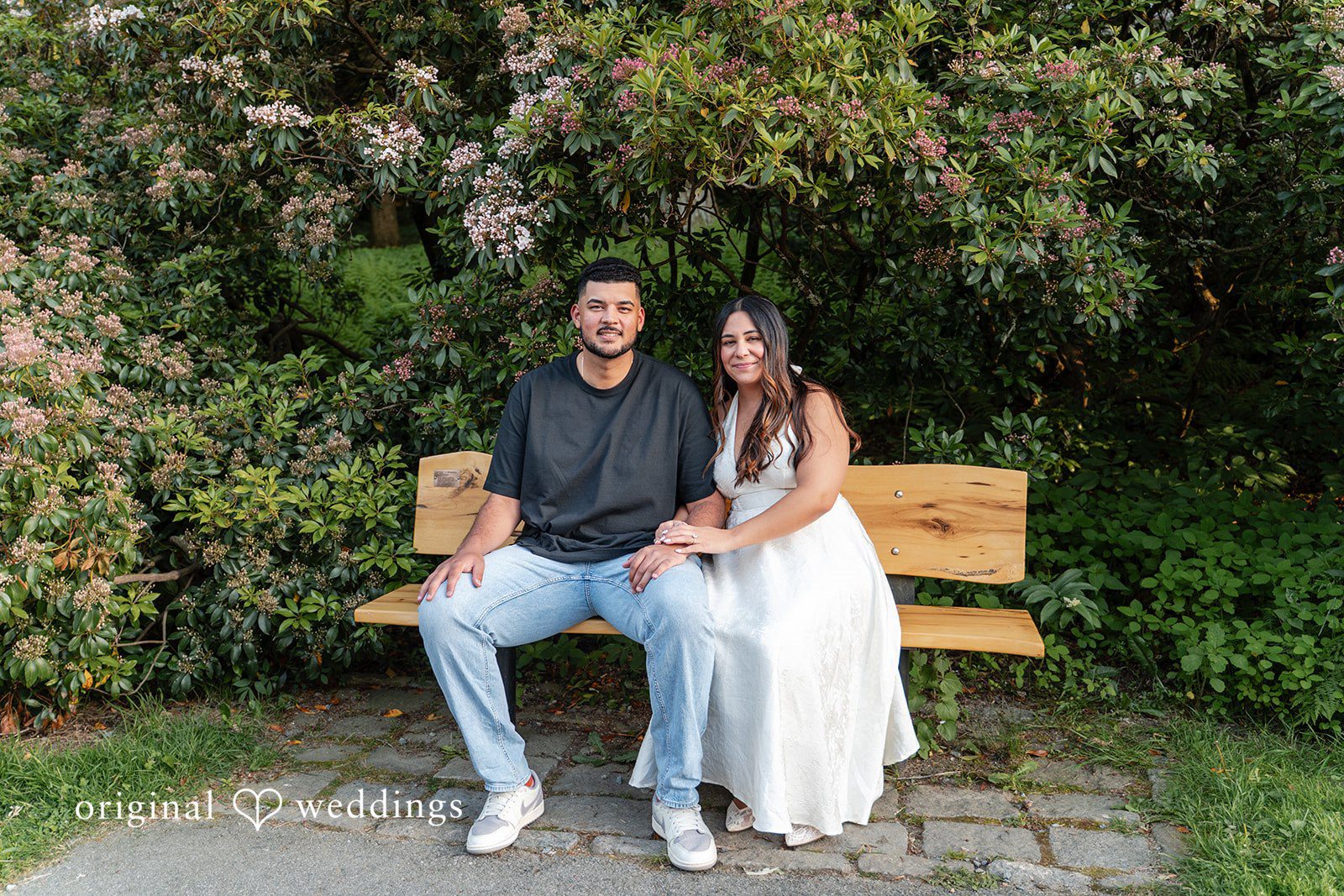 Anya + Max The couple sits together on a garden bench surrounded by blooming greenery
