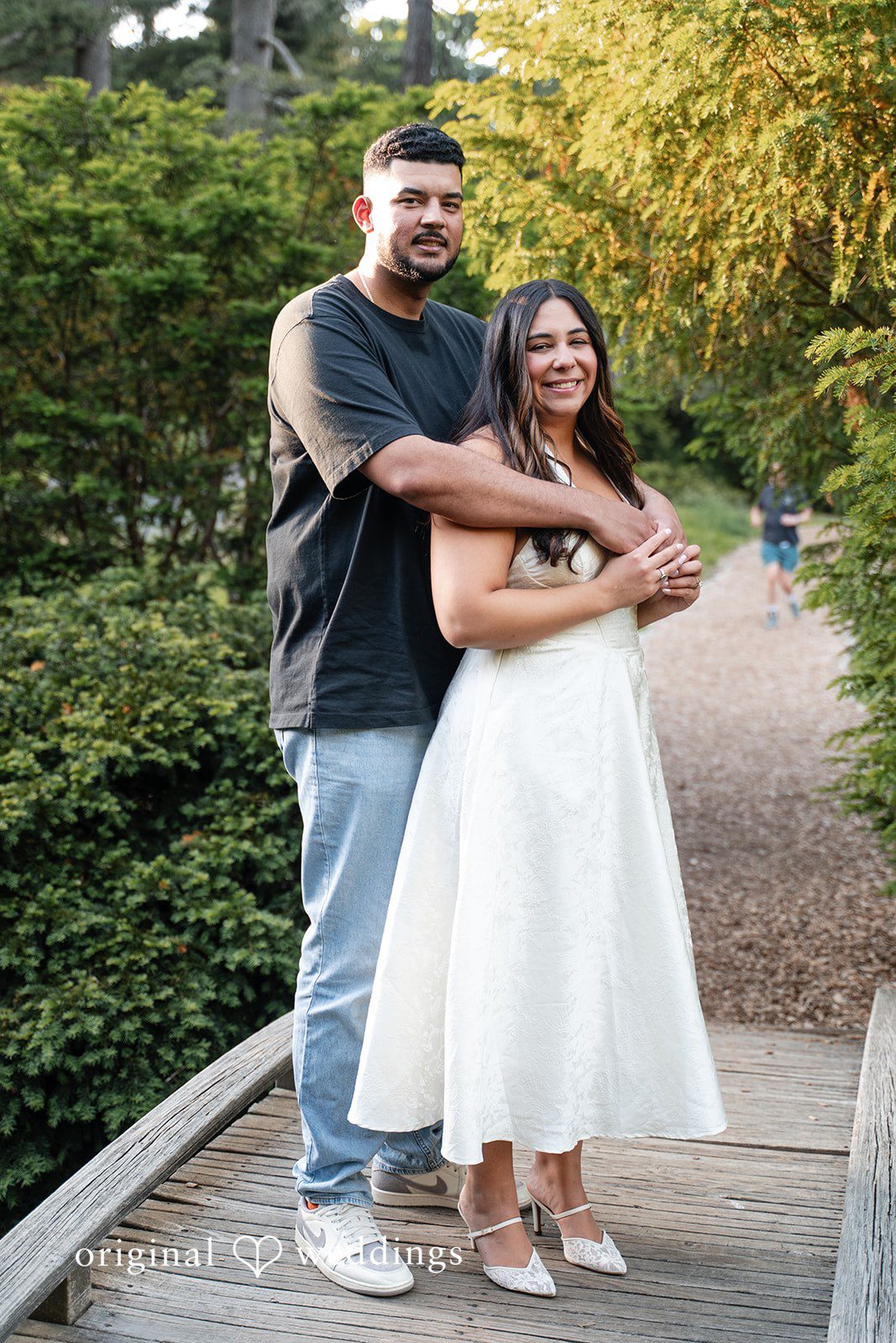 Anya + Max The couple shares a warm embrace on a wooden bridge during their engagement session at Arnold Arboretum captured by Boston engagement photographers from Original Weddings.