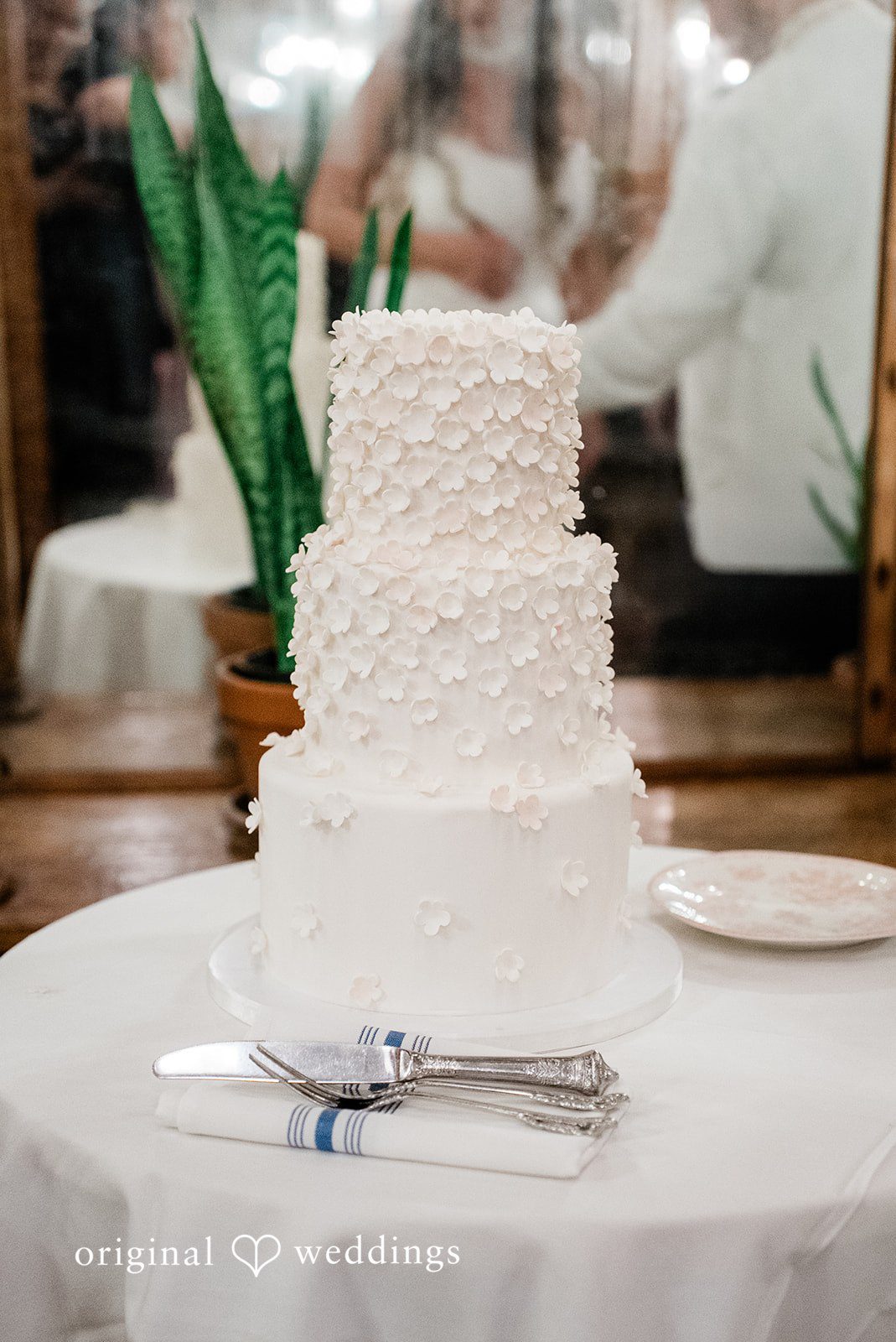 Michael + Maria An elegant three-tier white wedding cake adorned with delicate floral details at Beatnik on the River.
