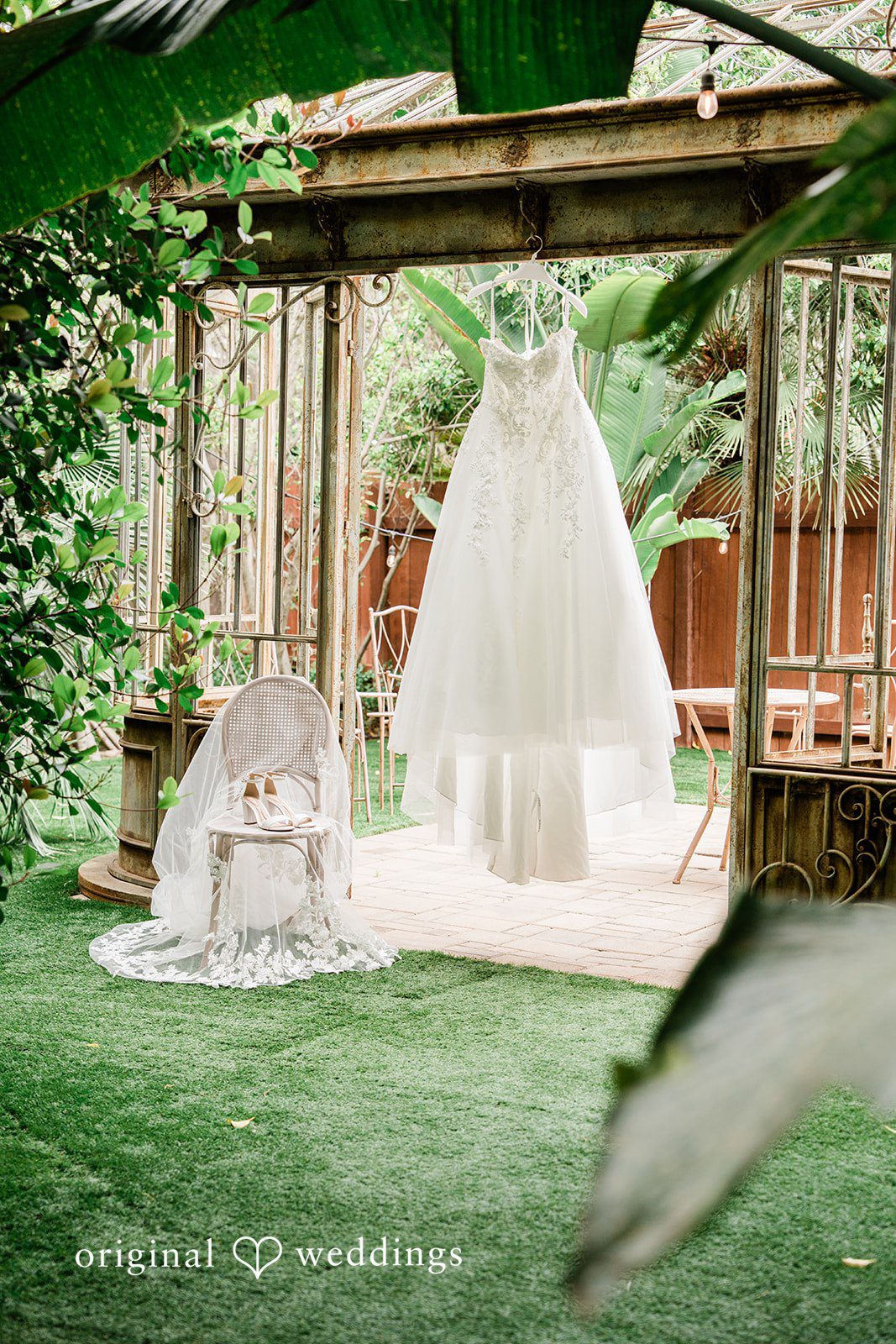 Mae + Nicholas Wedding dress hanging inside Botanica’s lush greenhouse setting.