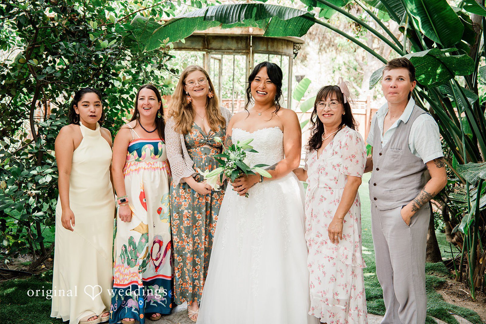 Mae + Nicholas Bride posing with family and friends in Botanica’s lush tropical garden.