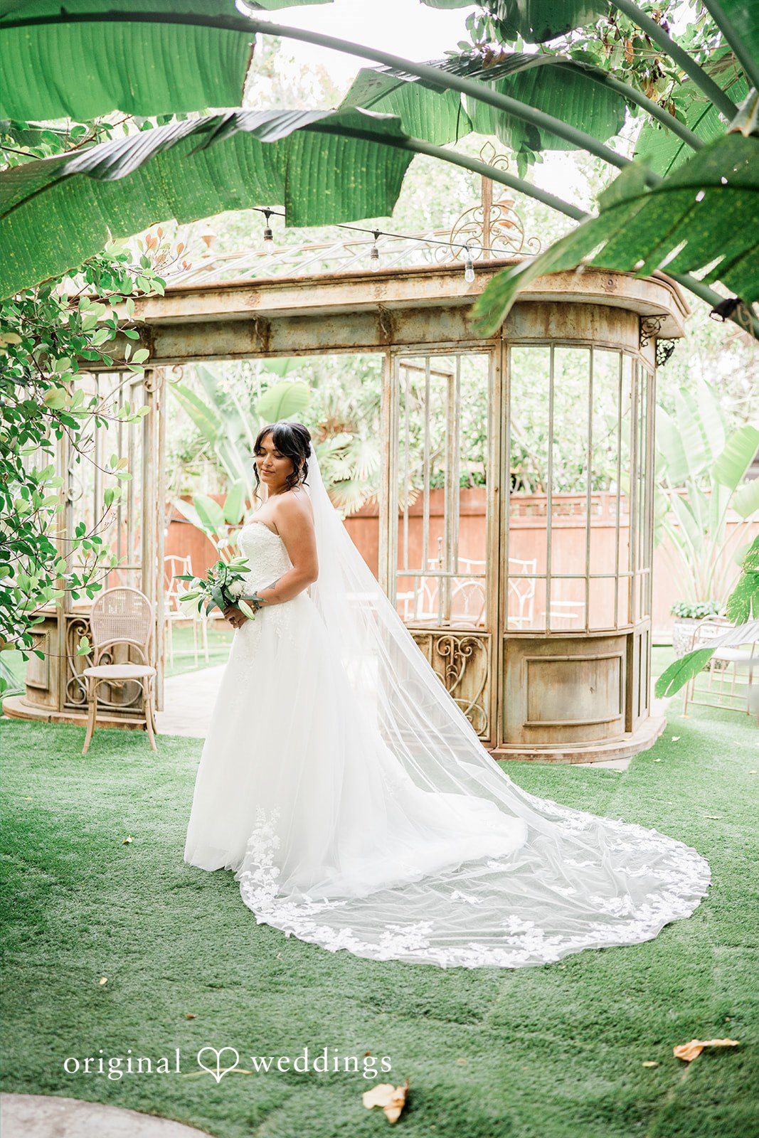 Mae + Nicholas Bride posing in Botanica’s greenhouse garden with her flowing veil and bouquet.