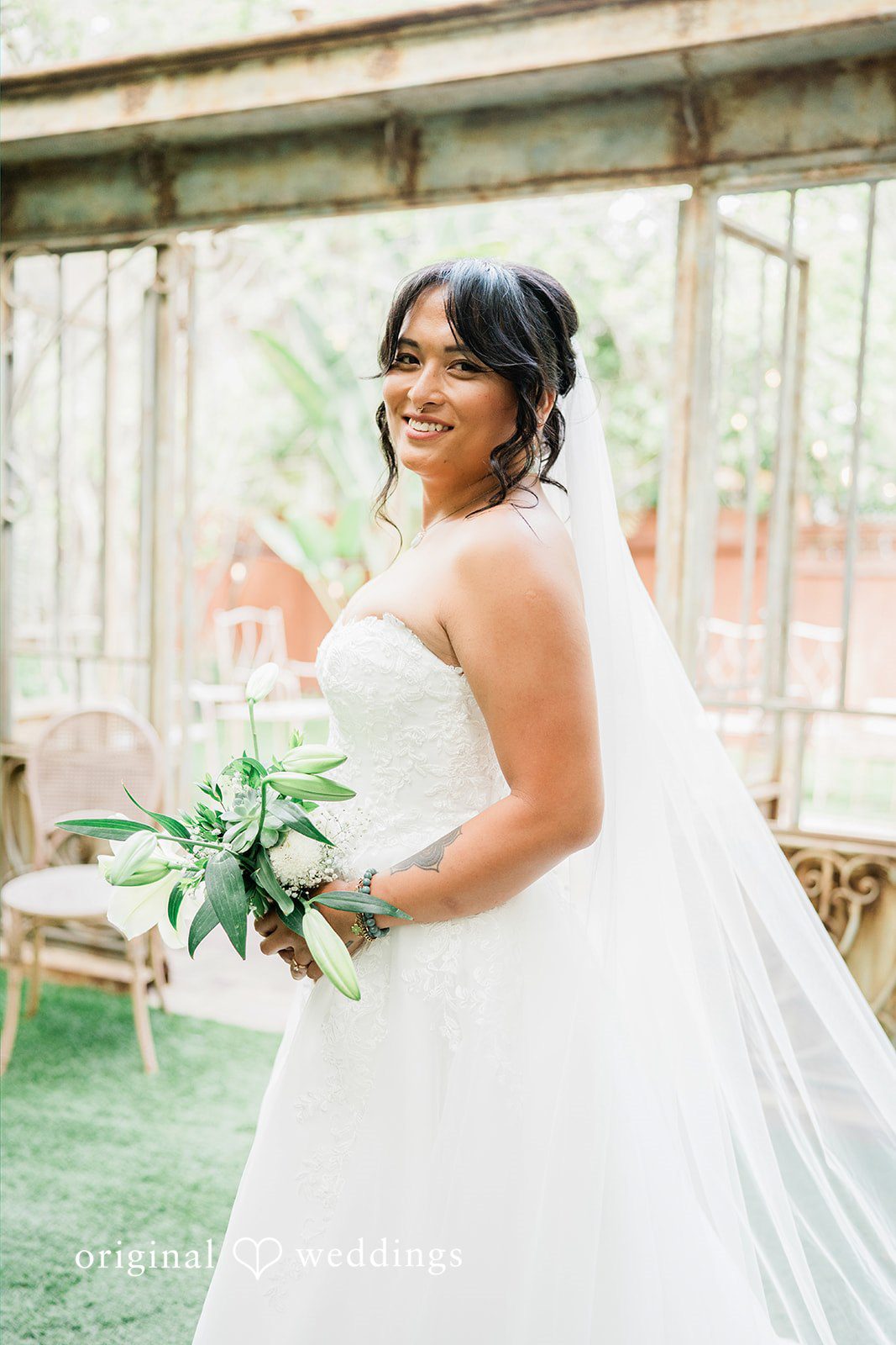 Mae + Nicholas Smiling bride portrait at Botanica holding a white lily bouquet.