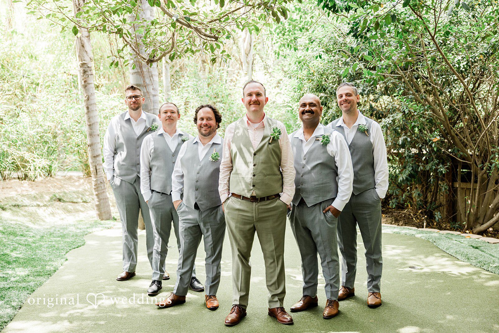 Mae + Nicholas Groom posing with his groomsmen in Botanica’s lush garden walkway.