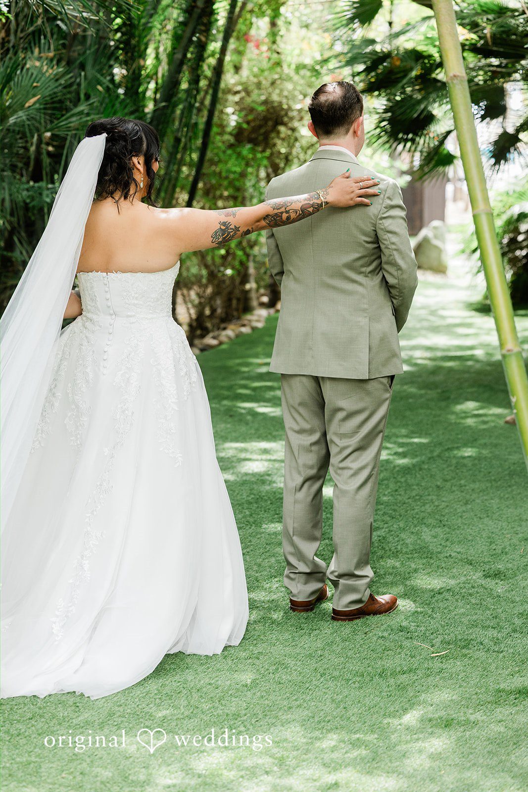 Mae + Nicholas Bride taps groom’s shoulder for a first look in Botanica’s bamboo-lined garden path.