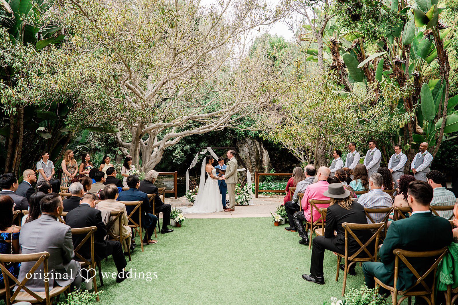 Mae + Nicholas Wide view of the wedding ceremony at Botanica surrounded by lush greenery and guests.