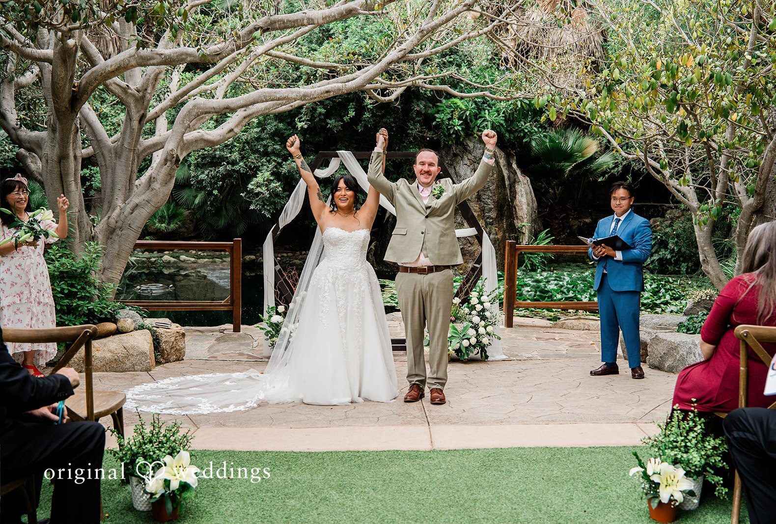 San Diego wedding photography from Original Weddings capturing the bride and groom celebrating their marriage at Botanica with joyful raised hands.