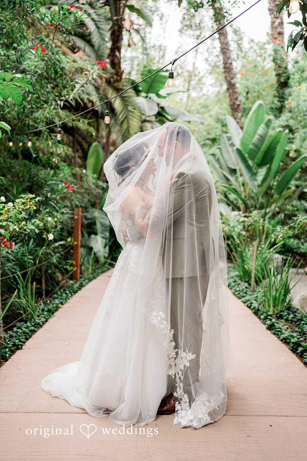 Mae + Nicholas Newlyweds sharing a romantic veil portrait along Botanica’s tropical walkway.
