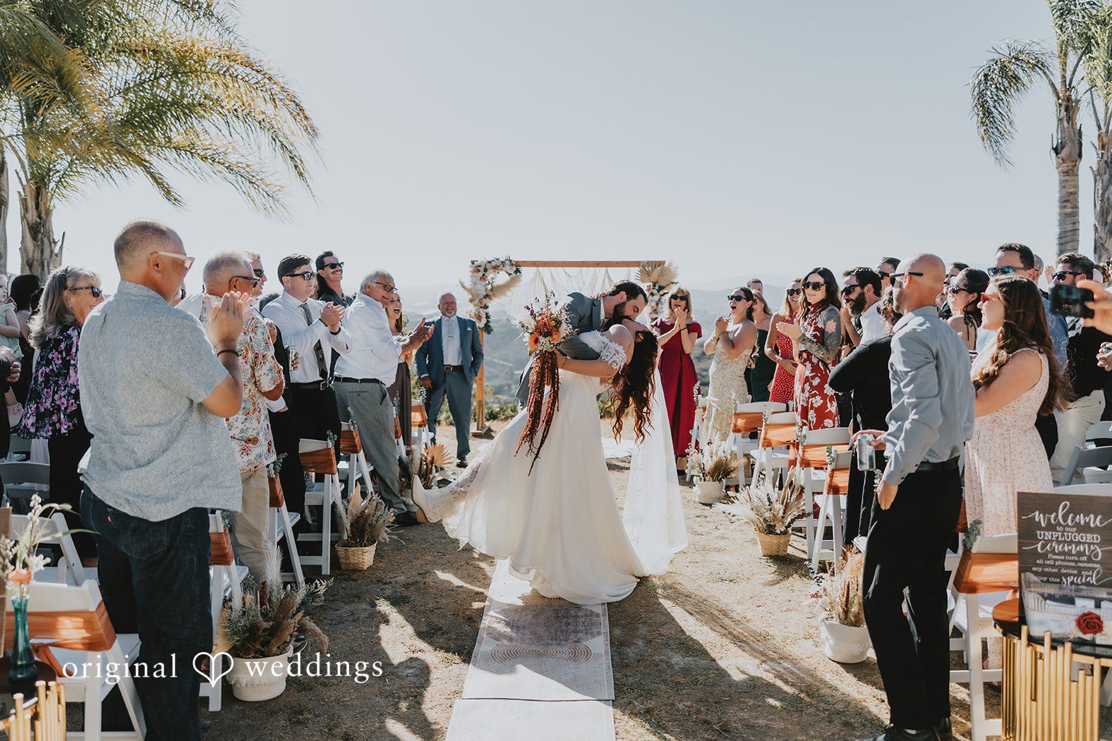 Bride and groom sharing a romantic kiss while guests cheering around