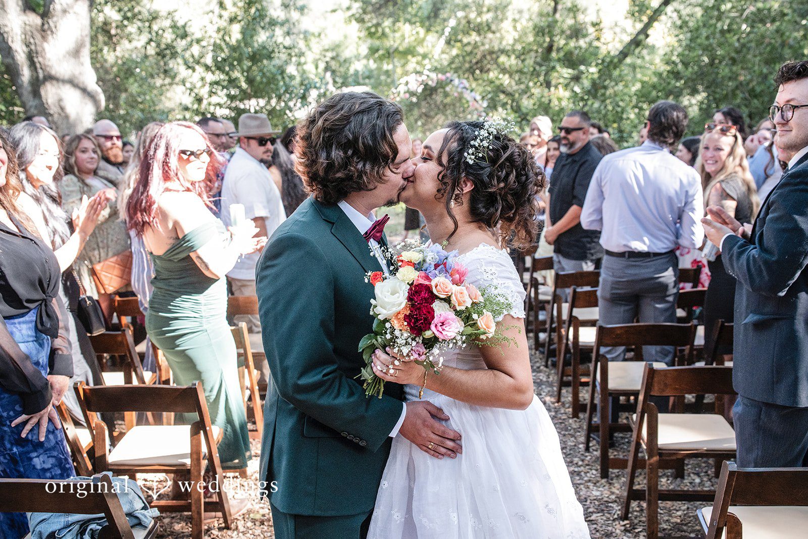 Keely + Sam Bride and groom sharing a kiss with the guests around, cheering.