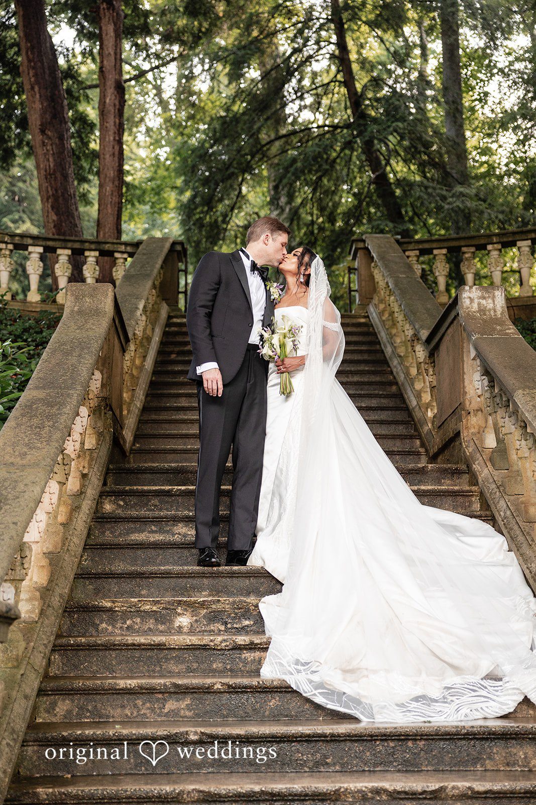 Bride and groom share a kiss on a grand stone staircase at Cater at Woolford