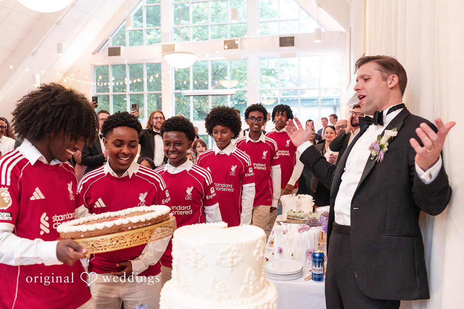 Groom reacts with surprise as guests in matching red jerseys present a special performance at the reception