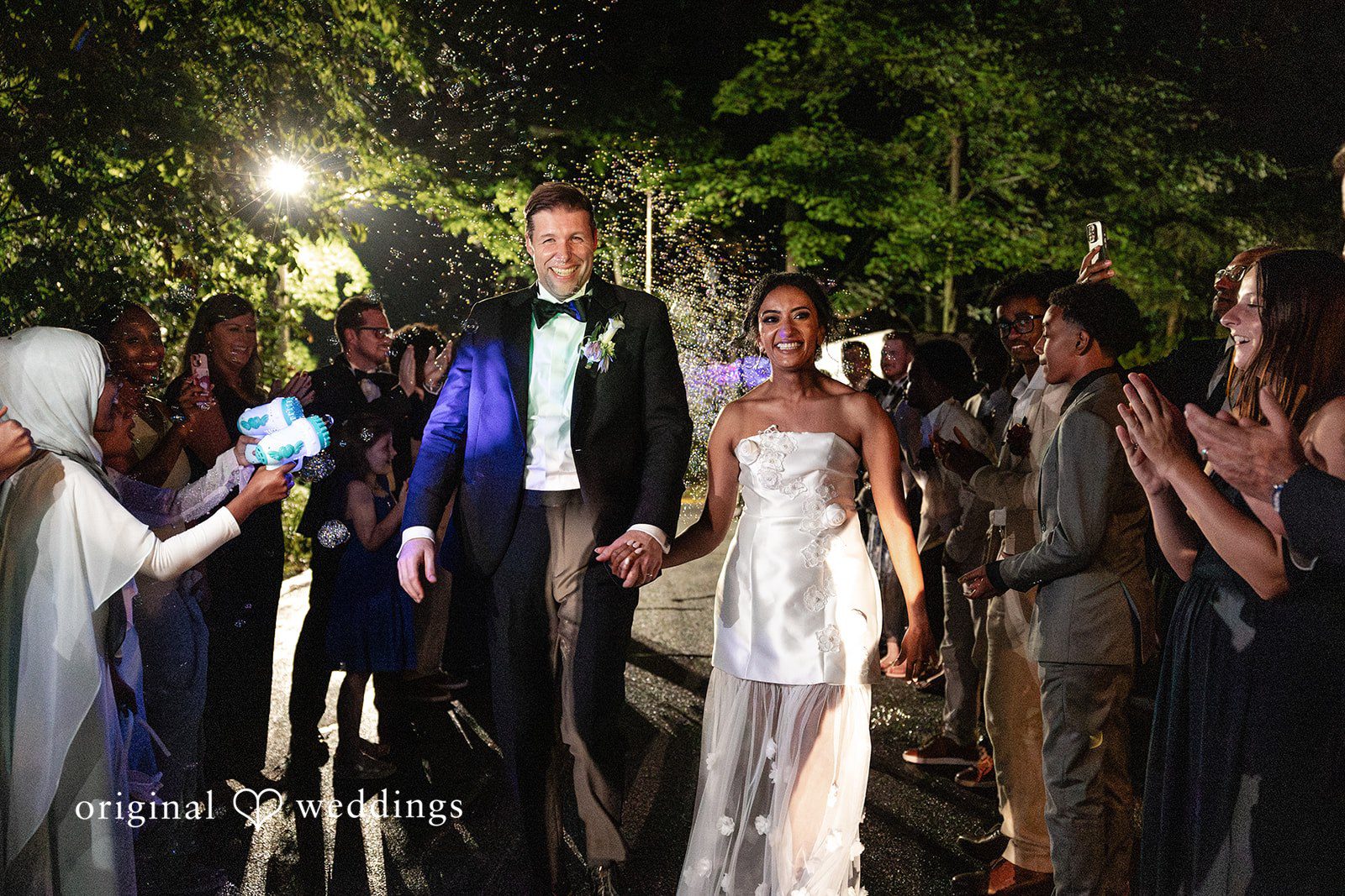 Newlyweds walk hand in hand through bubbles during a magical nighttime send-off at Cator at Woolford captured by Atlanta Wedding Photographers from Original Weddings