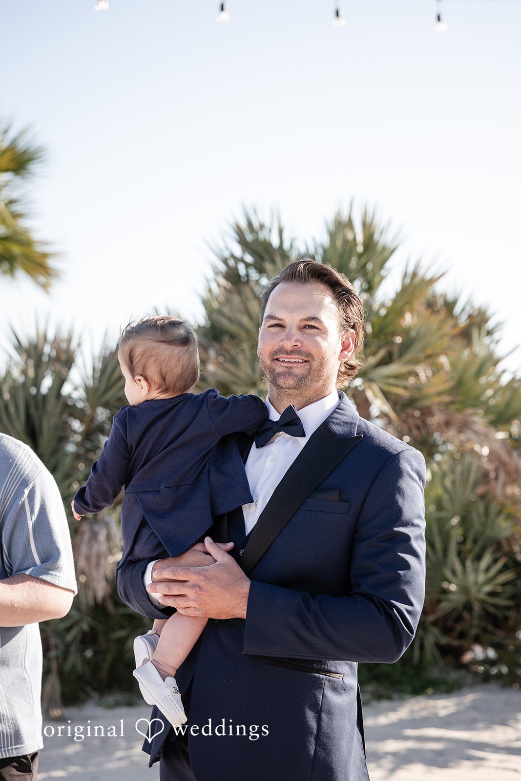Kellie + AJ Groom holding a baby during a candid wedding moment
