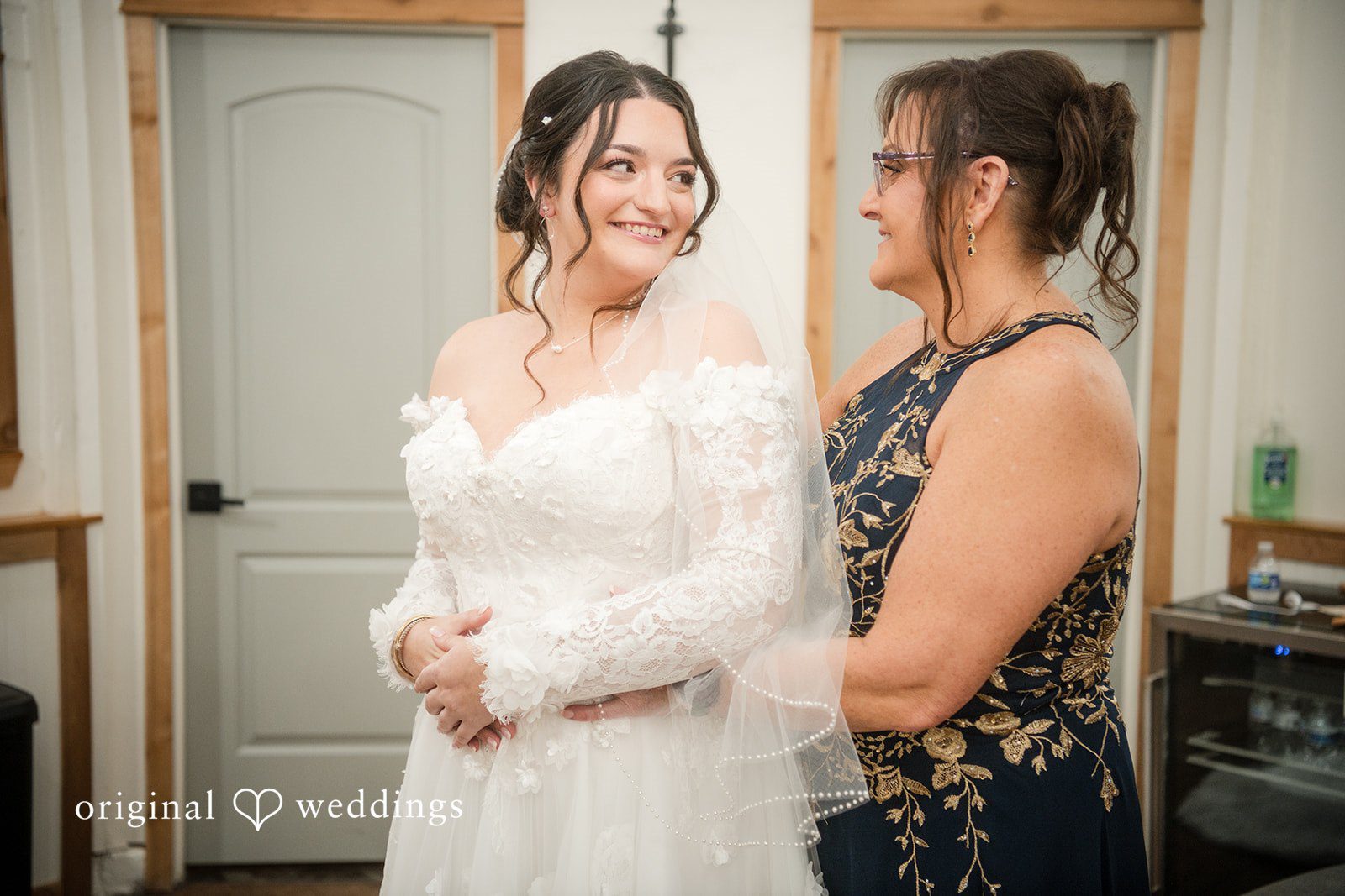 Natalie + Dakin Smiling bride in a lace wedding dress facing a woman in a dark sleeveless dress.